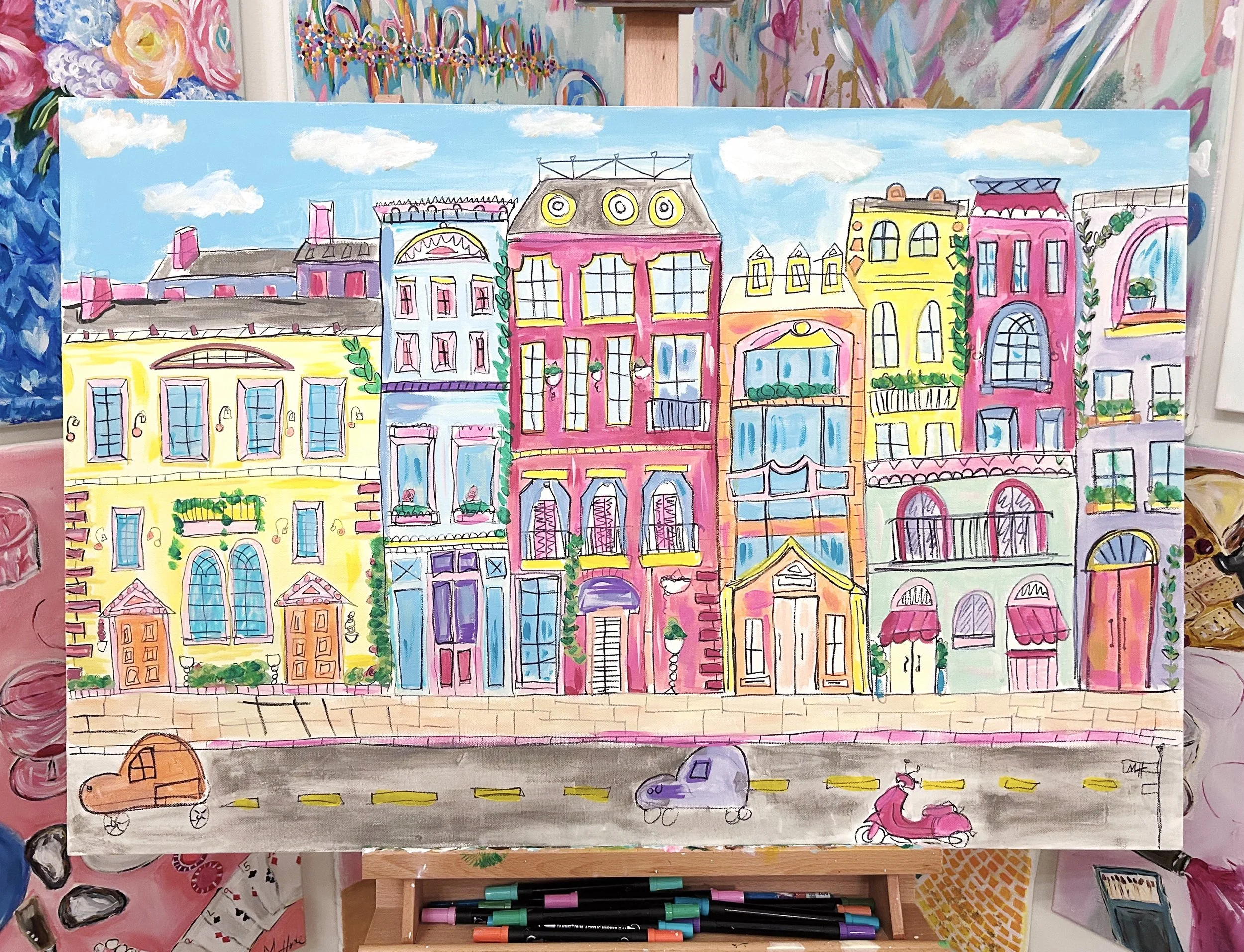 A colorful painting of a cityscape with various buildings in pink, yellow, purple, green, and orange, with a street and cars and a scooter in the foreground. The sky is blue with white clouds.