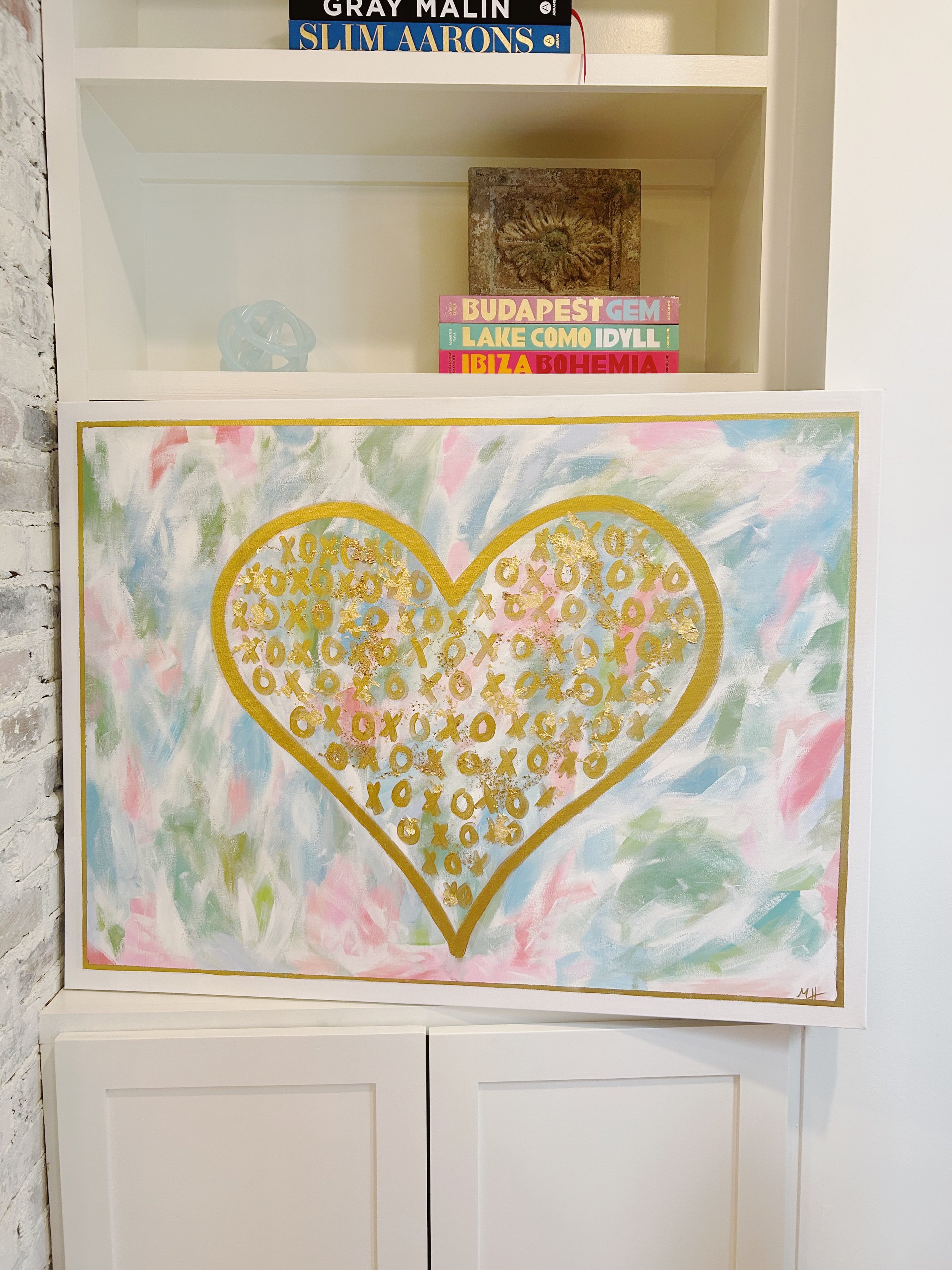 A colorful abstract painting of a gold-outlined heart filled with gold XO symbols, set against a pastel, brushstroke background of pink, green, blue, and white.