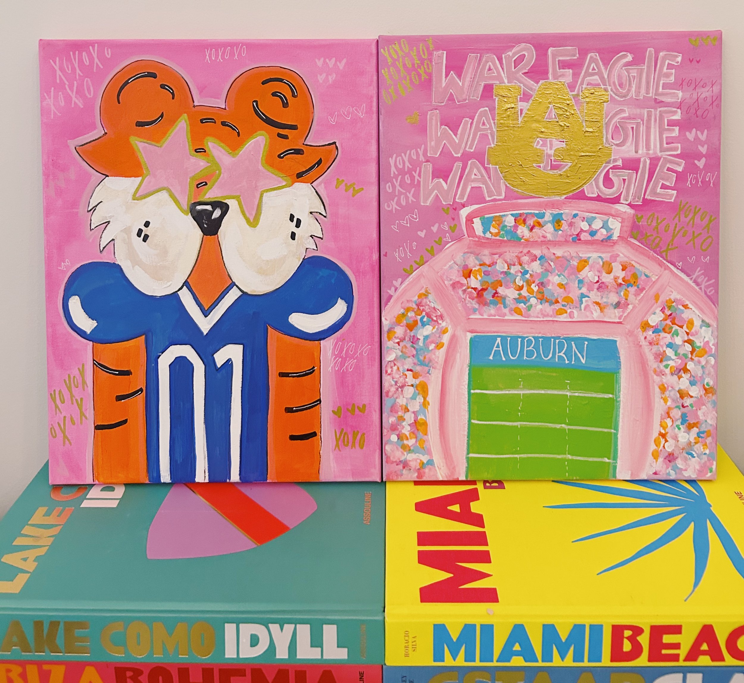 Painting of a dog wearing a sports jersey with the number 01, with star-shaped eyes, on a pink background. Next to it is a colorful stadium scene with the word 'AUBURN' on a green field, and the words 'WAR EAGLE' above it. The artwork is displayed ab