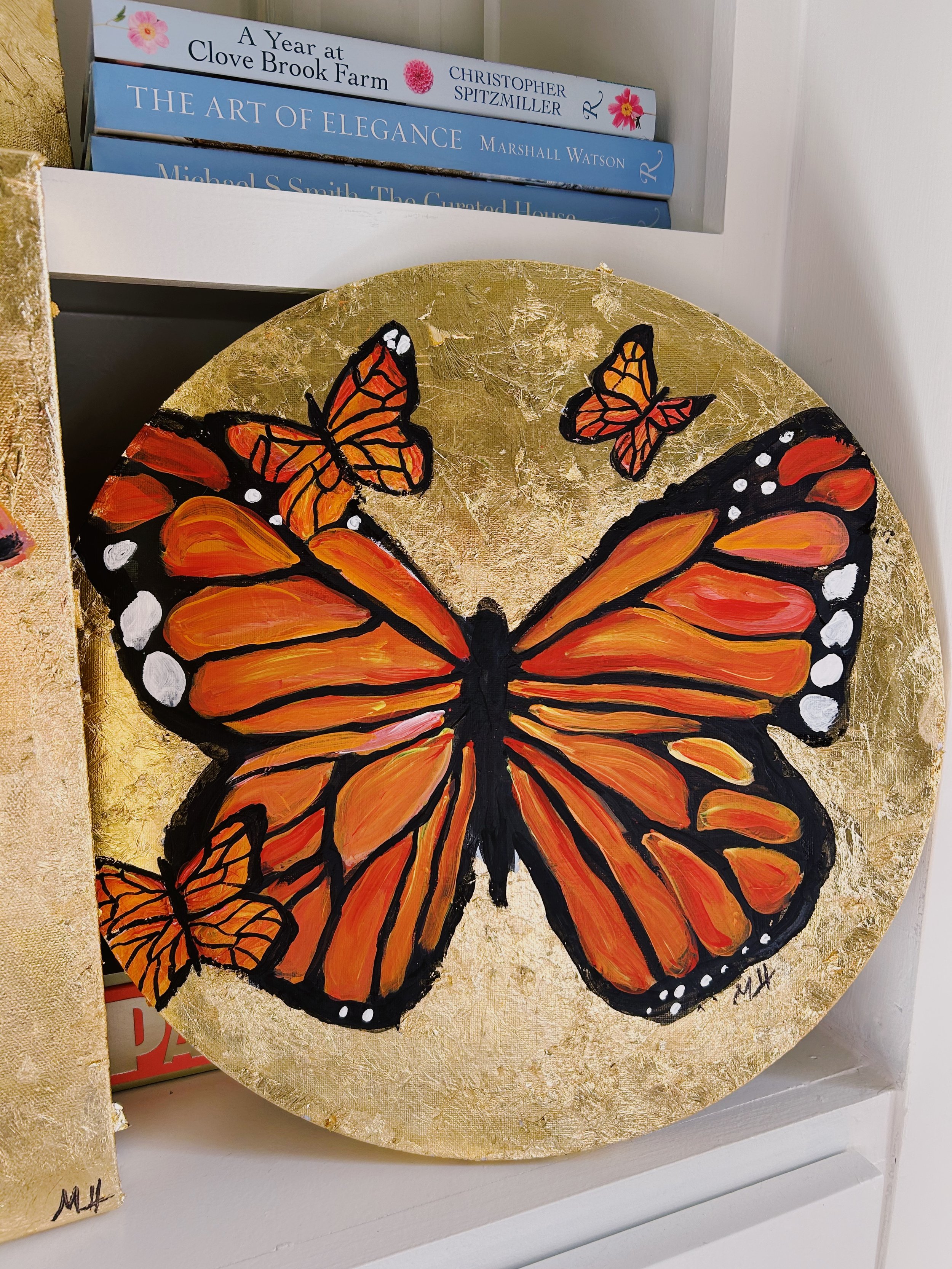 Painting of a monarch butterfly with orange and black wings and white spots, accompanied by smaller butterflies, against a gold background.