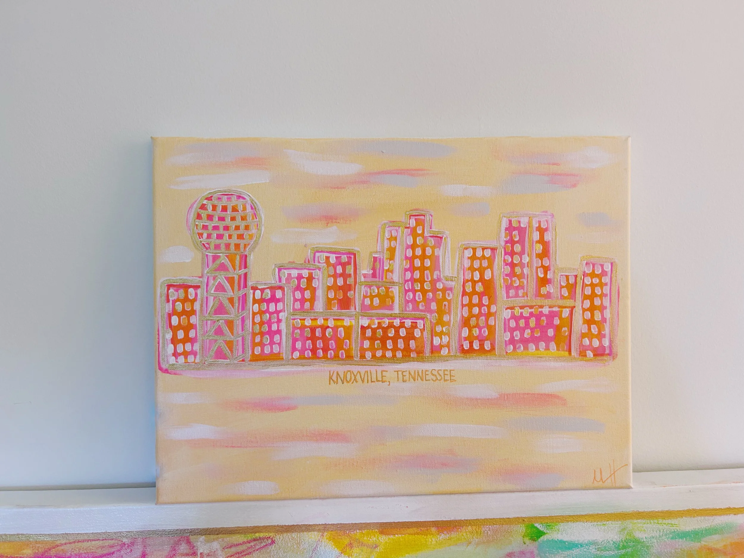 A colorful painting of the Knoxville, Tennessee skyline with pink and orange hues, featuring prominent buildings and the Sunsphere, on a light background.