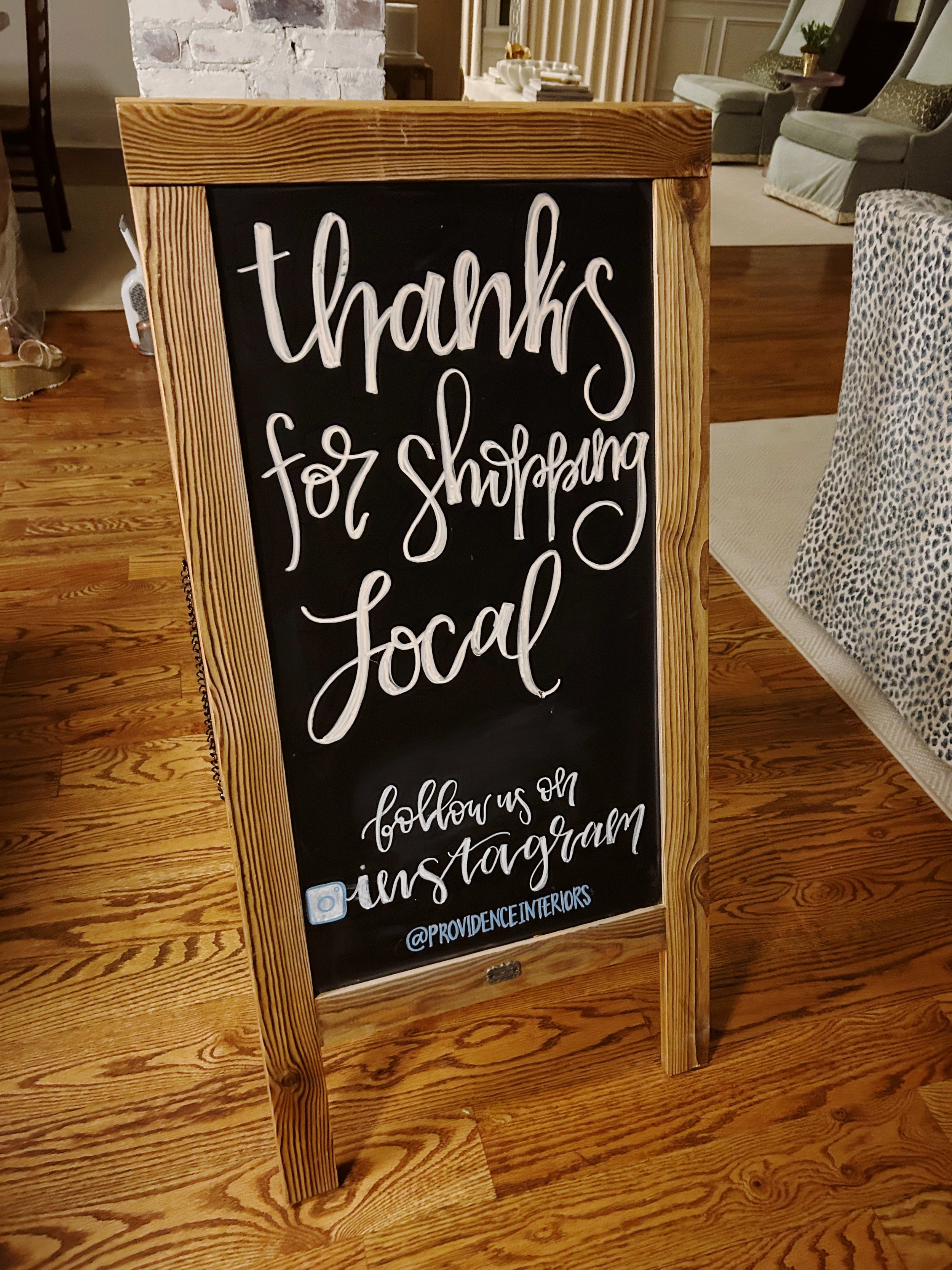 A chalkboard sign with a wooden frame that says "thanks for shopping local" and "follow us on Instagram @PROVIDENCEINTERIORS."