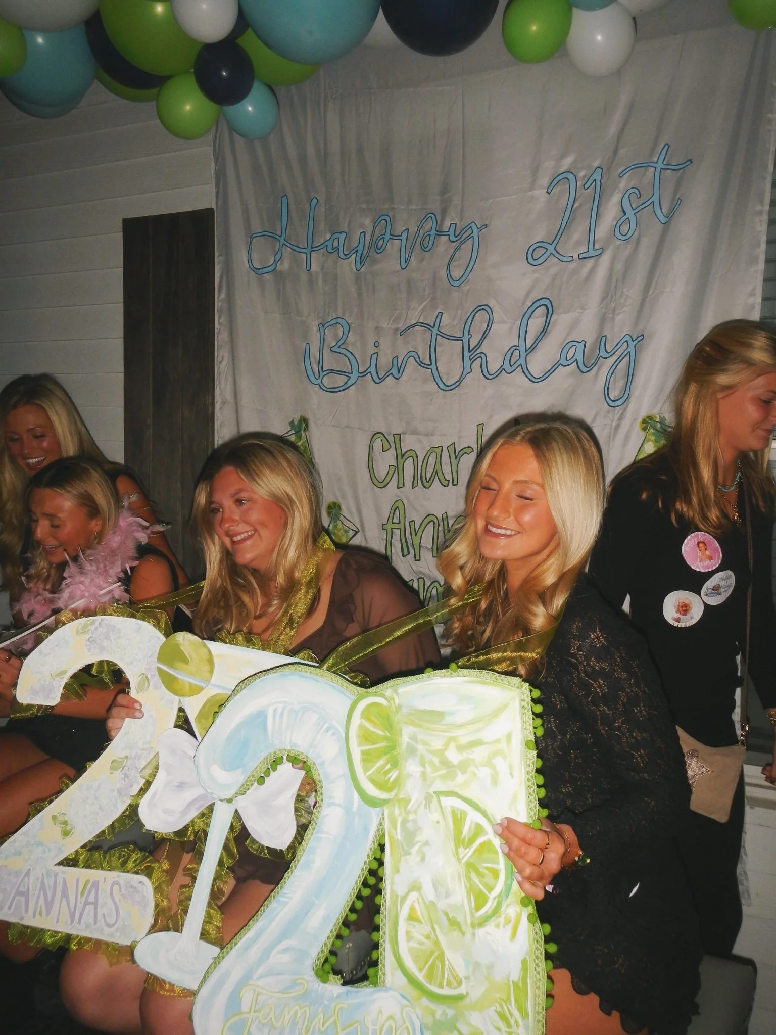 Group of women celebrating a 21st birthday party, with a large banner in the background and a birthday cake decorated with lime slices in the foreground.