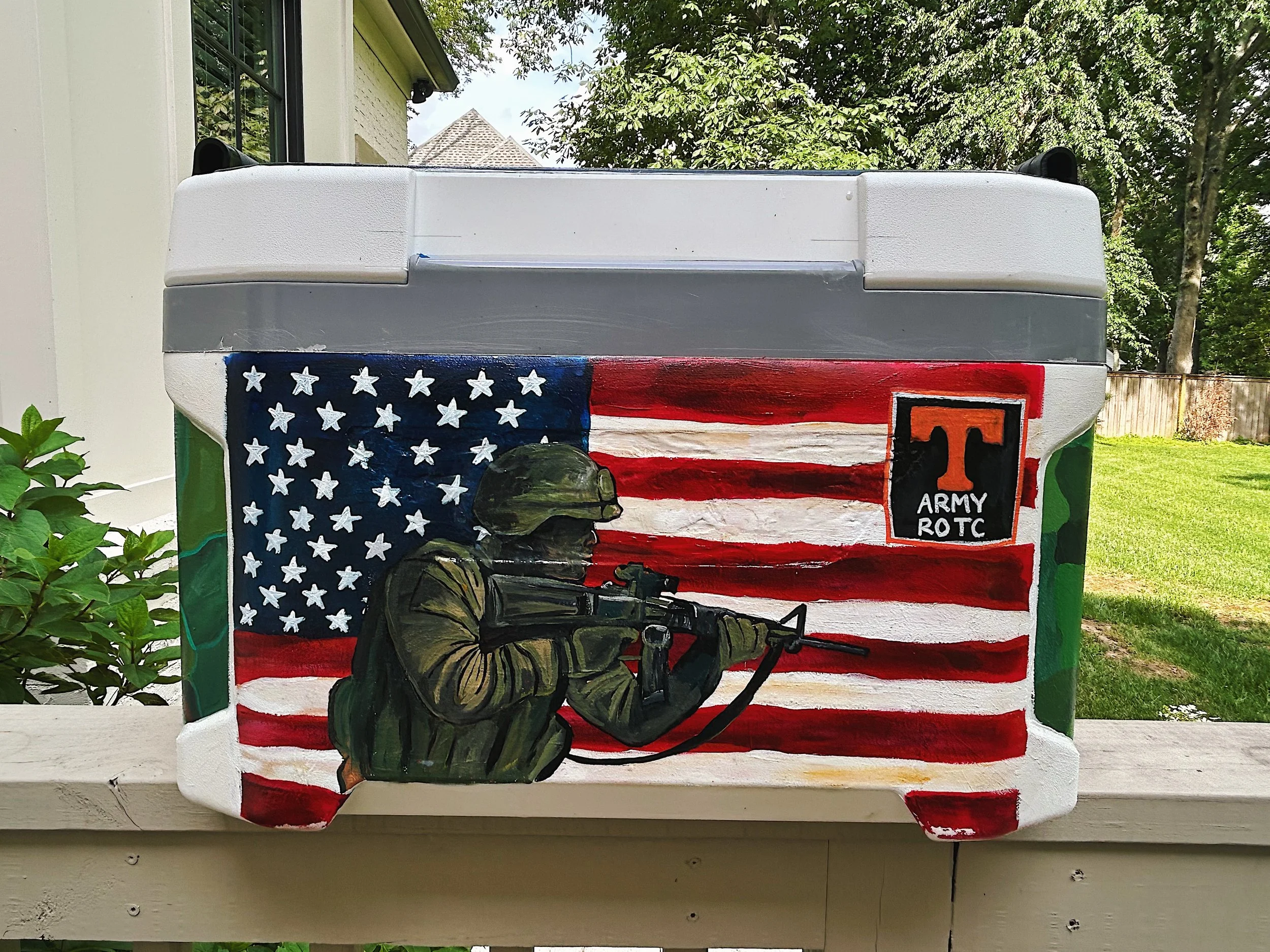 Hand-painted cooler featuring an American flag background, a soldier with a rifle, and a patch with a large orange T and the words "Army ROTC."
