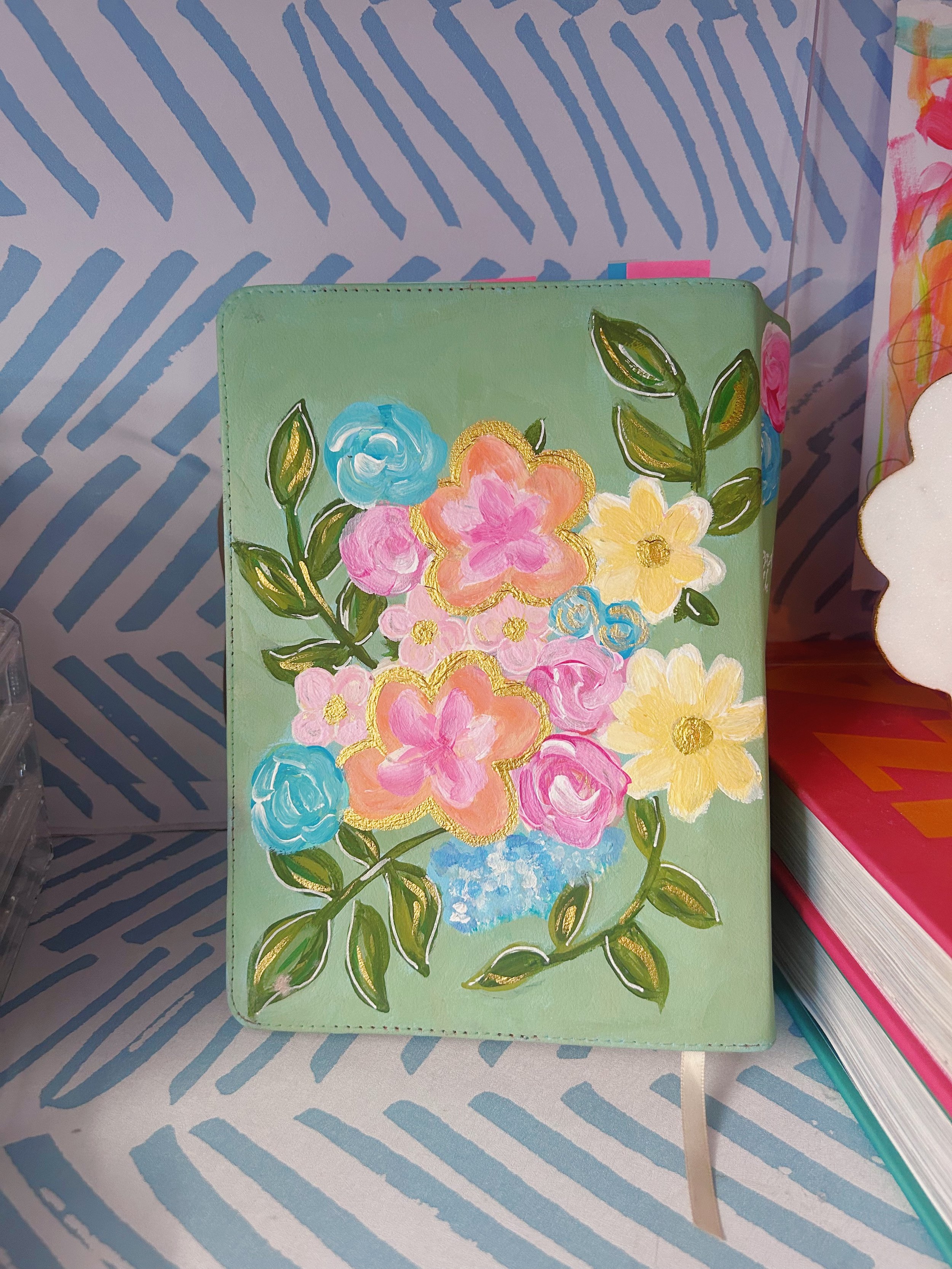 A colorful floral design with pink, blue, yellow, and peach flowers with green leaves painted on a light green background.