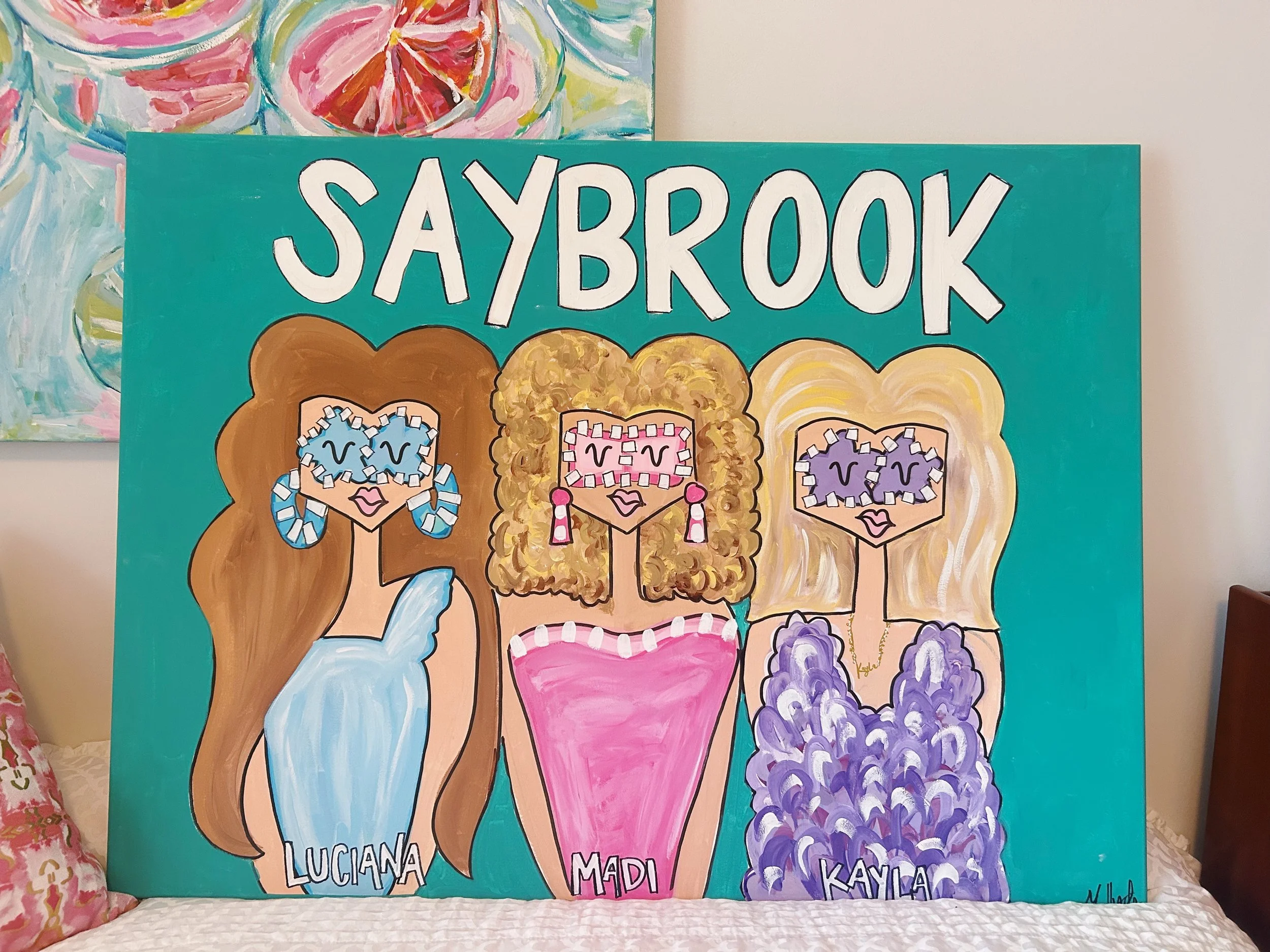 Colorful painting of three women with cartoonish faces, labeled Luciana, Madi, and Kayla, with floral and abstract backgrounds, and the title SAYBROOK at the top.
