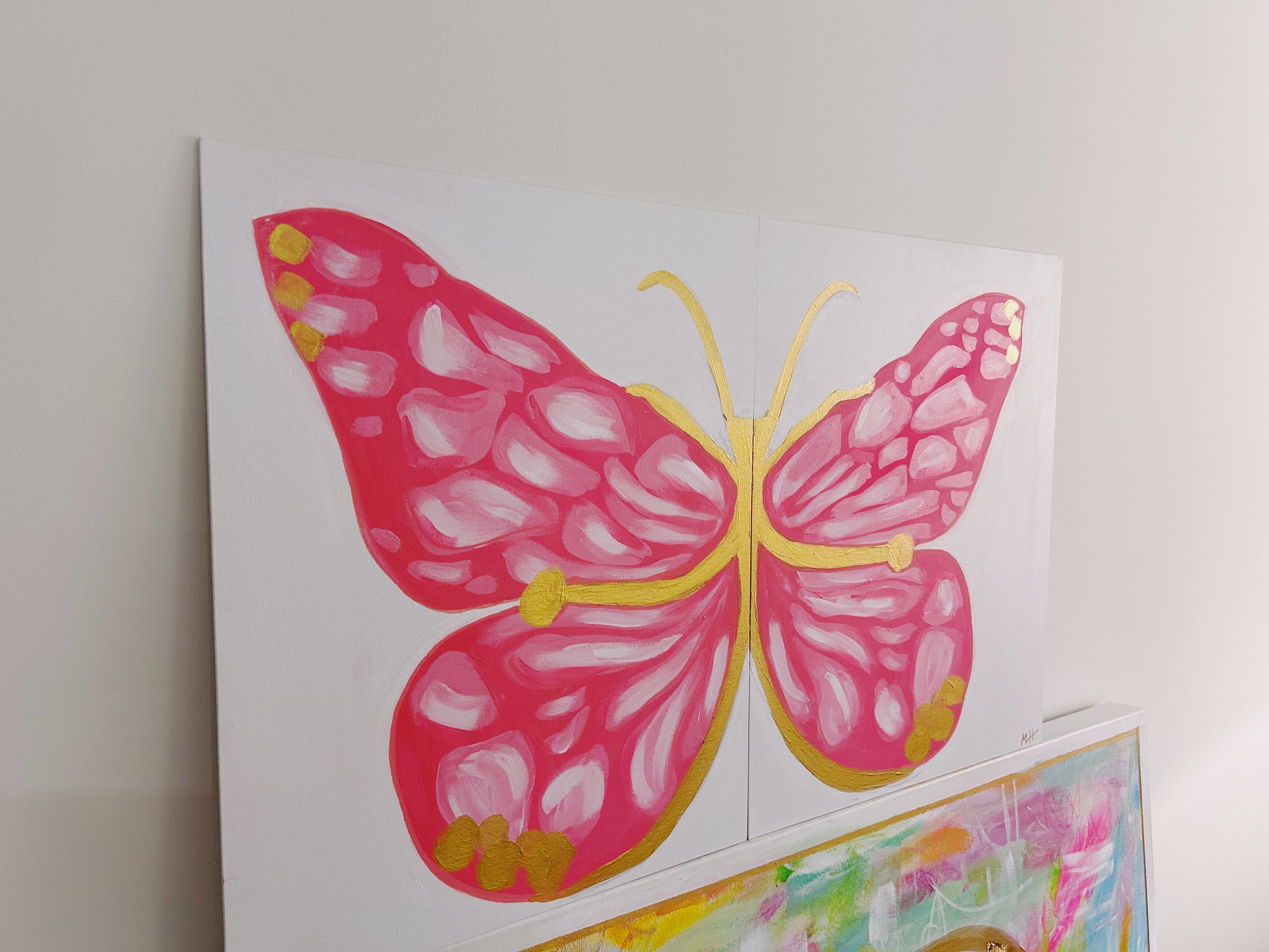 Pink butterfly artwork with gold accents on a white canvas wall.