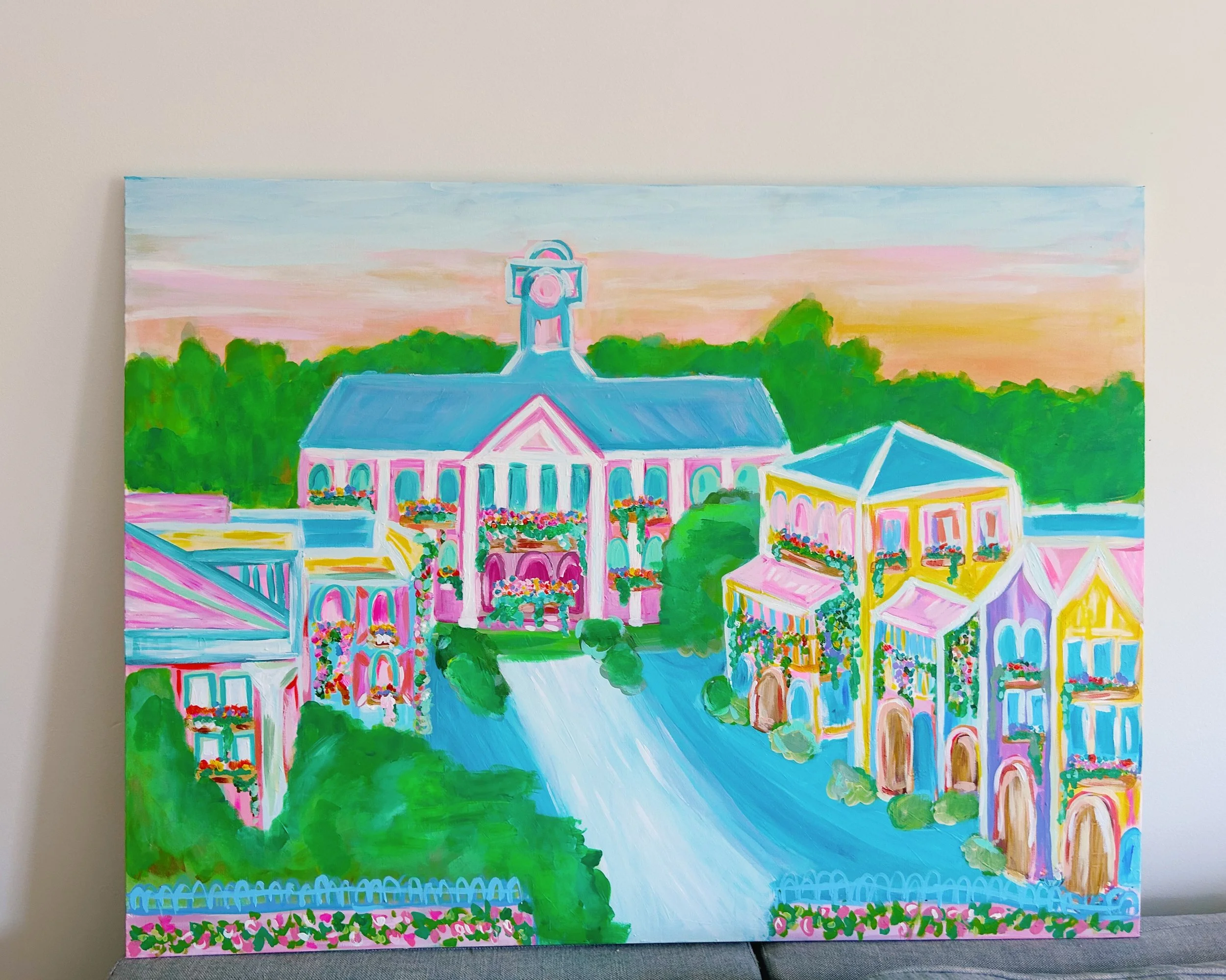 Colorful painting of a pastel-colored town with buildings decorated with flowers, a winding road, lush green trees, and a pink and blue sky at sunset.