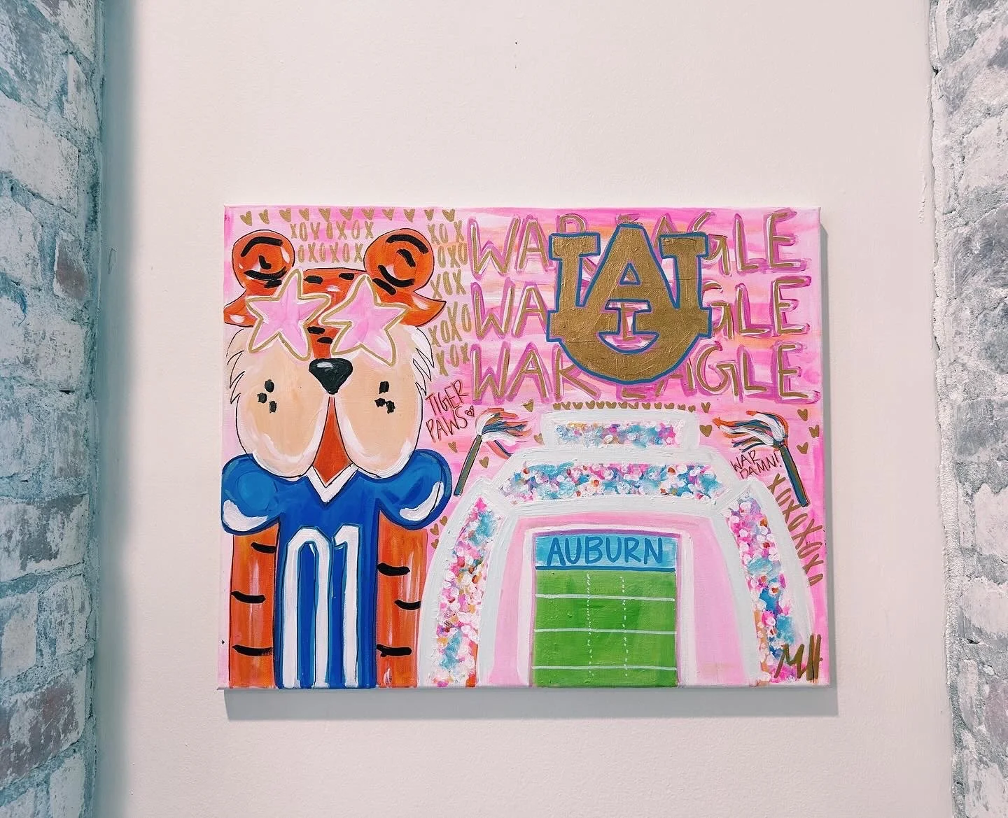 Artistic painting featuring a tiger mascot wearing a football jersey with the number 01, large pink star-shaped glasses, and a background decorated with pink, gold, and blue elements, including an Auburn University football stadium and school logo.