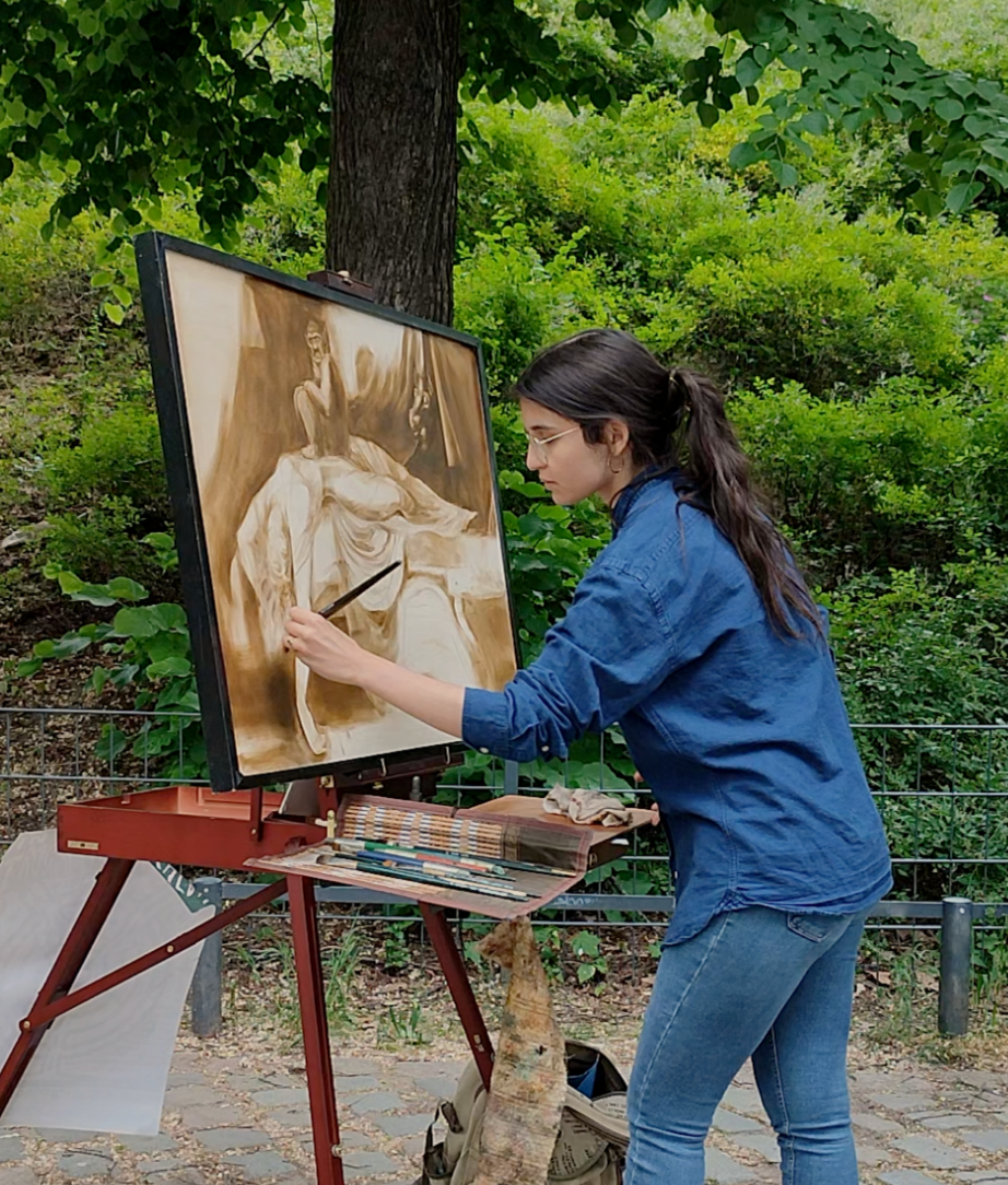 Young woman painting an image of a person on a canvas outdoors surrounded by green foliage.