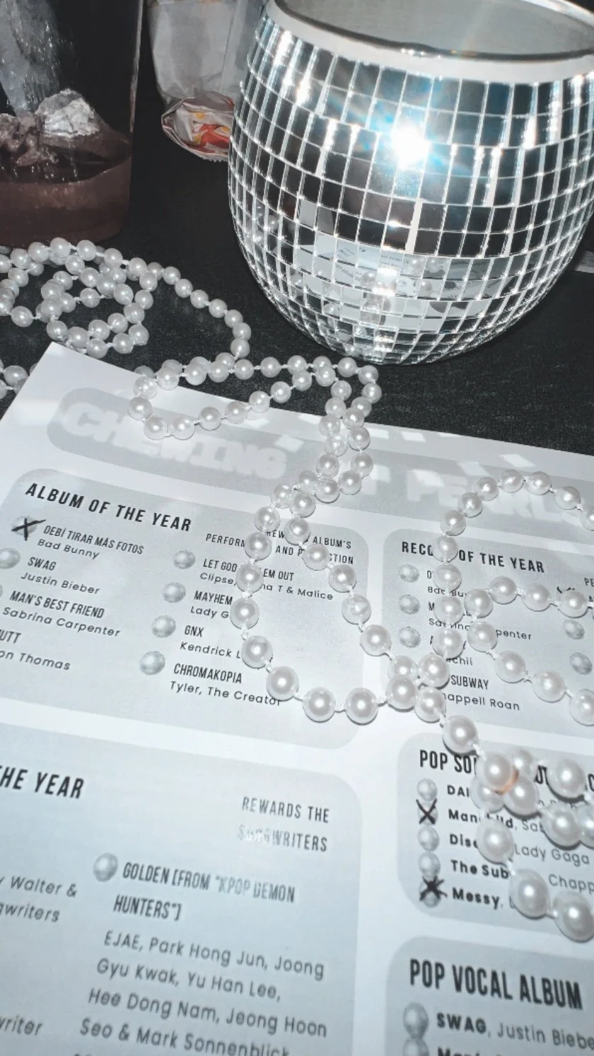 A shimmery disco ball, a string of white pearl beads, and a printed sheet of paper with text on a black surface.