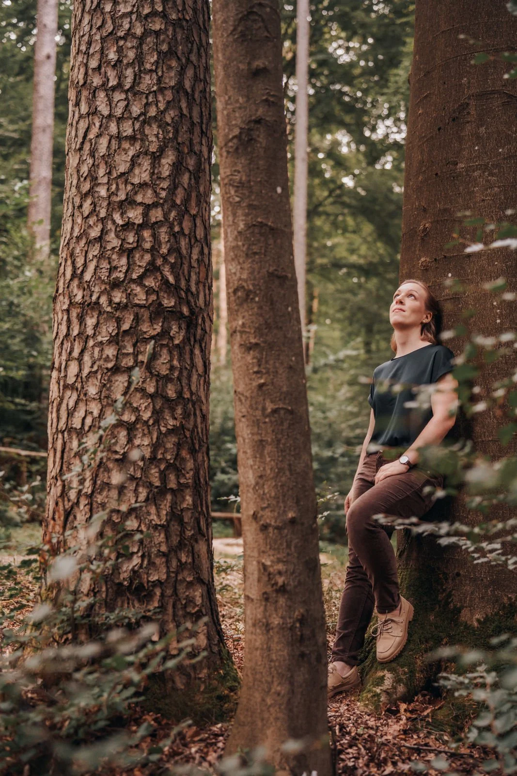 Patrizia Lehmann lehnt an einem Baum in einem Wald und schaut nach oben in den Himmel.