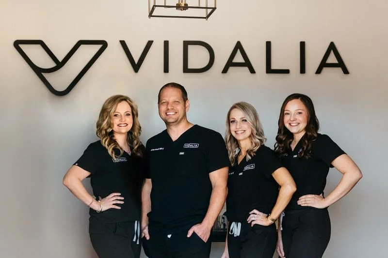 Four individuals wearing black VIDALIA uniforms standing in front of a wall with the VIDALIA logo, smiling at the camera.