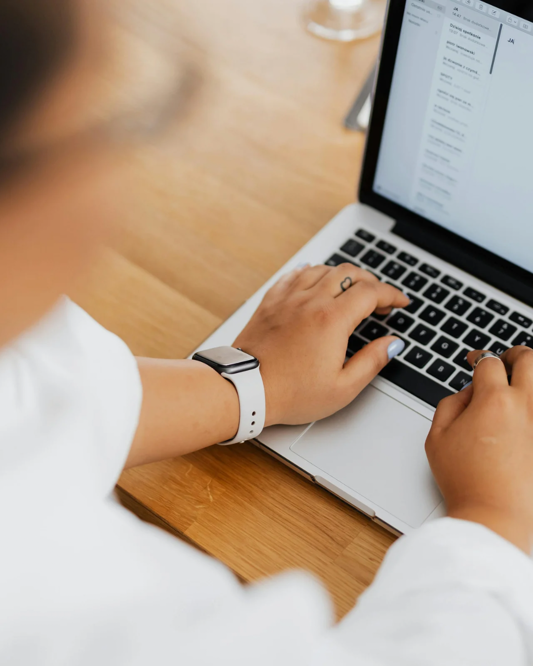 Persona che lavora al laptop, indossa un orologio intelligente e un anello, scrive sulla tastiera in un ambiente luminoso.