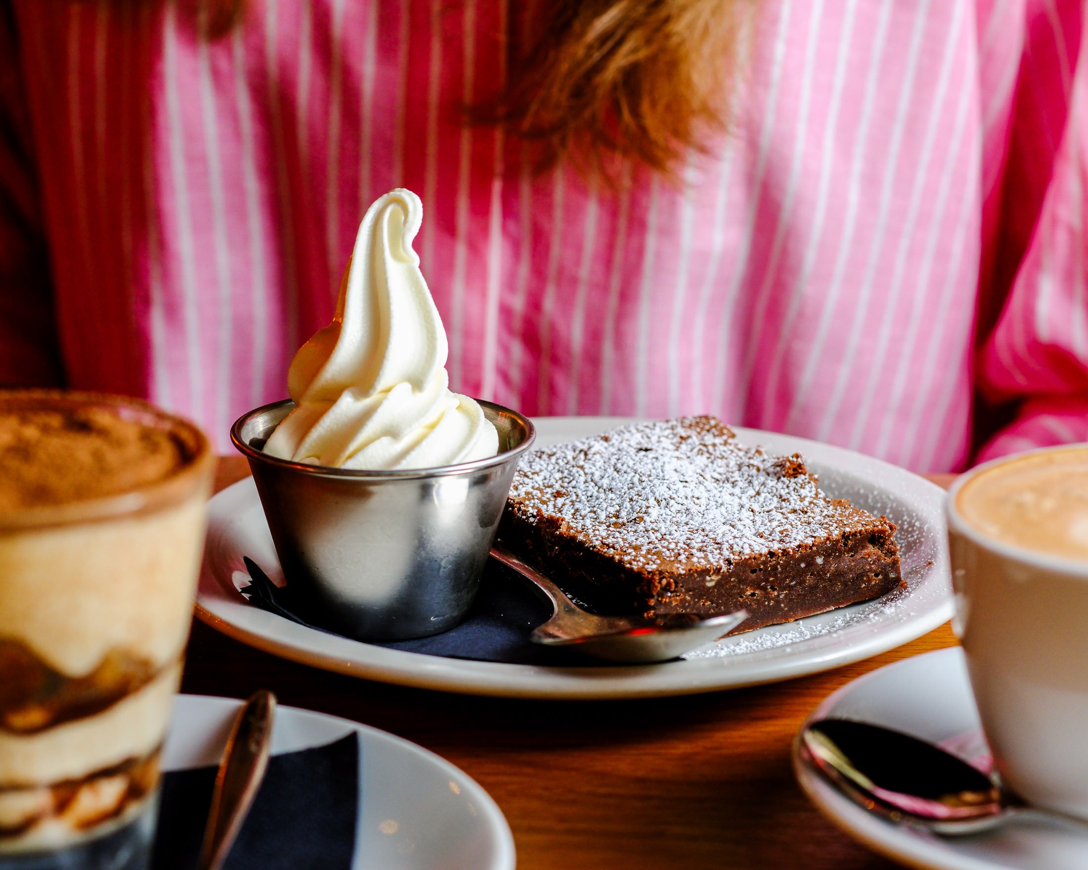 A man with glasses and a red cap is holding a pizza peel with a freshly baked pizza, in front of a pizza oven.