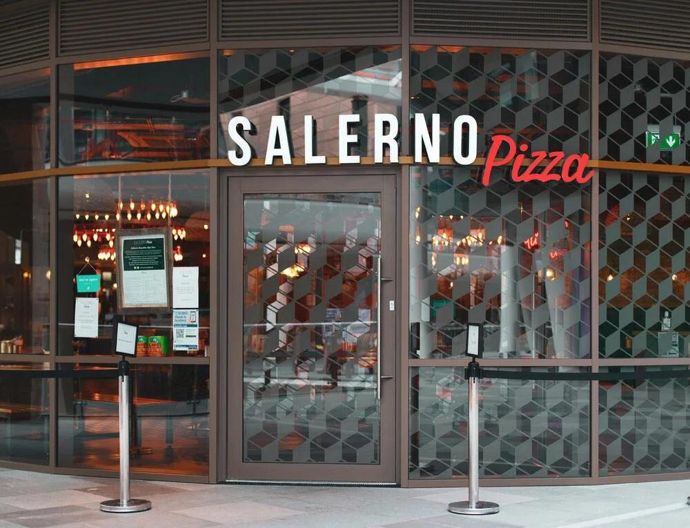 Front of a Salerno Pizza restaurant with glass windows and door, modern geometric design, and a menu display outside.