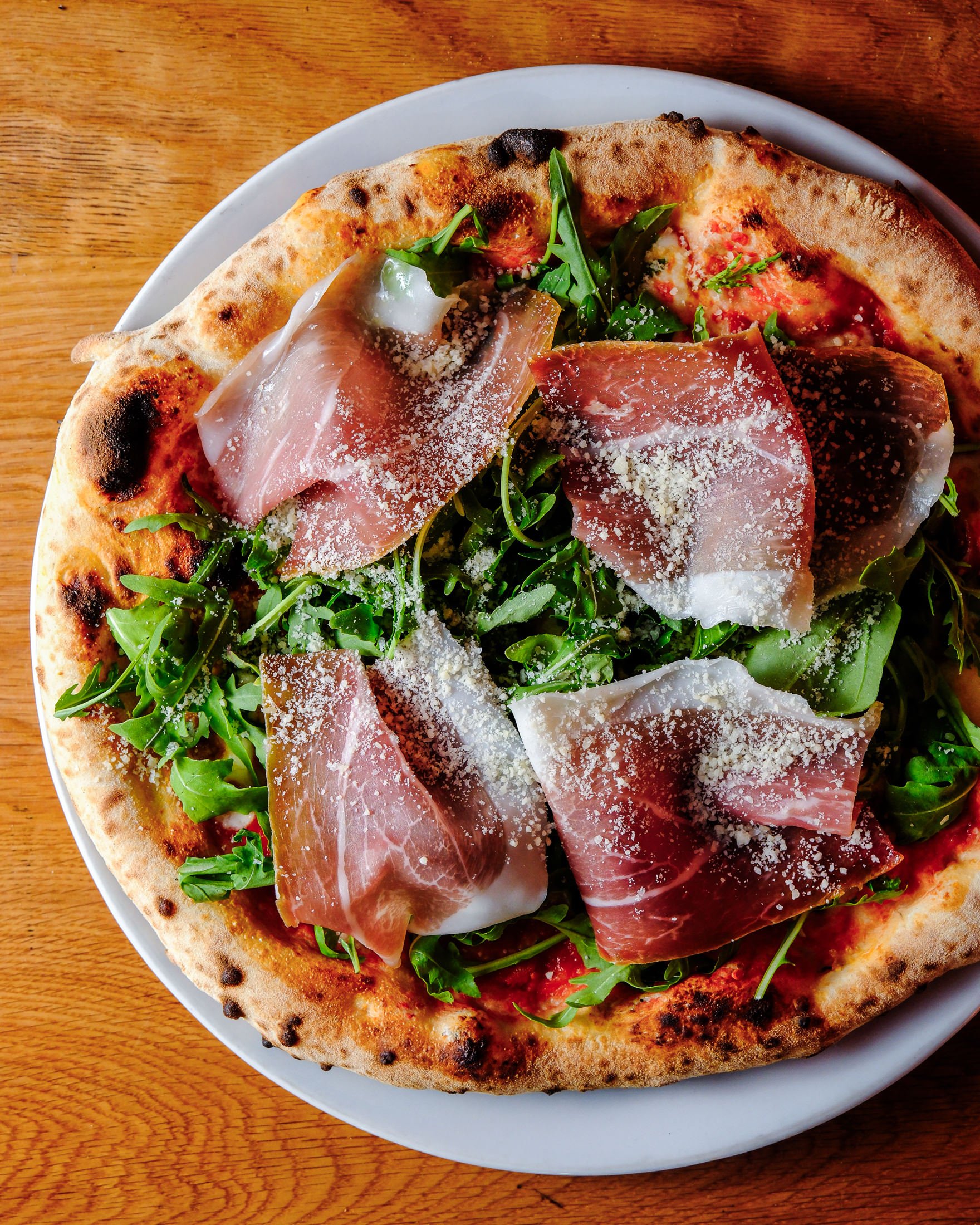 Salerno Pizza restaurant interior showing exposed brick walls and wooden tables set with placemats and metallic containers. Modern chandelier and wicker pendant lights hang from the ceiling.