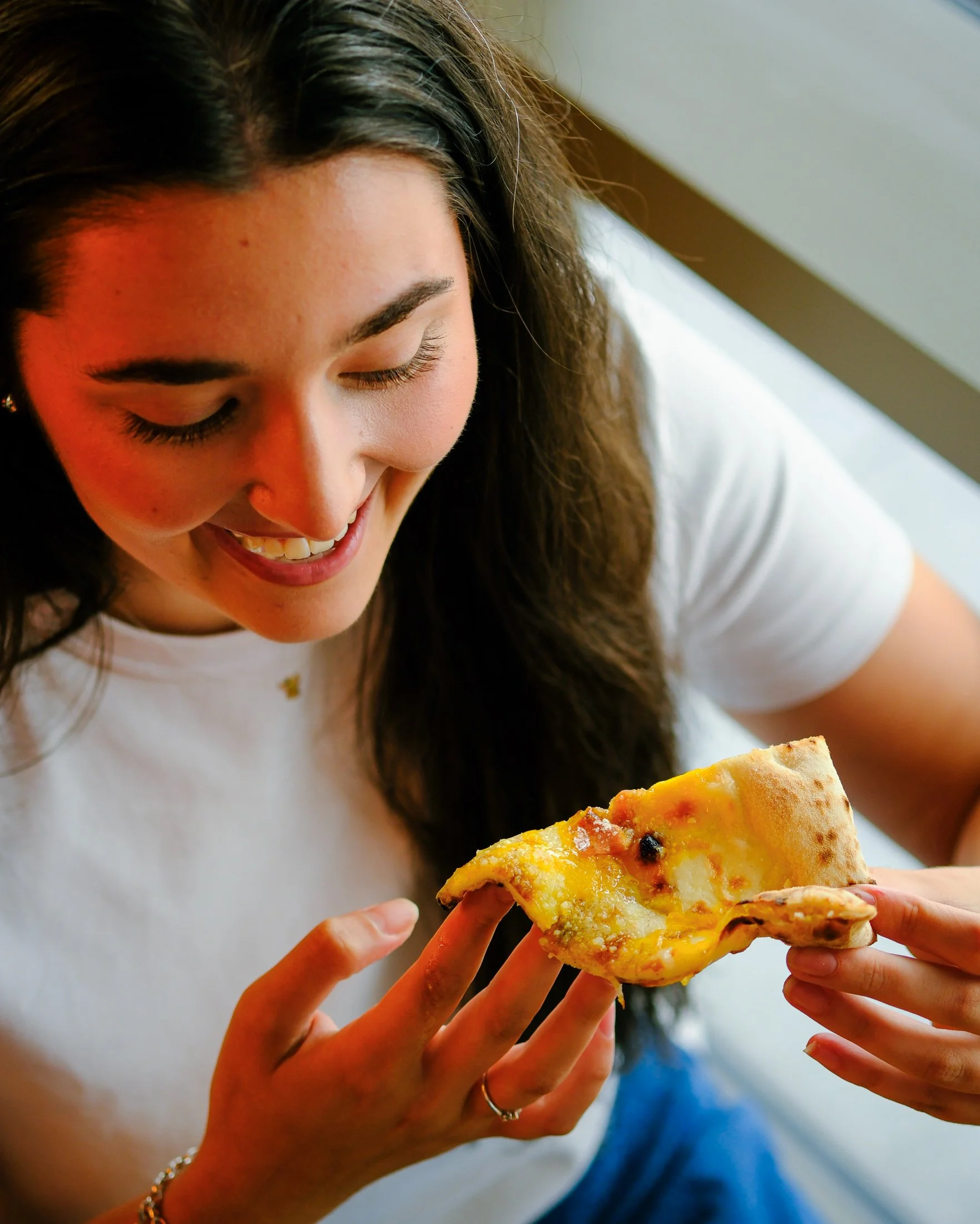 A woman smiling while holding a slice of pizza.