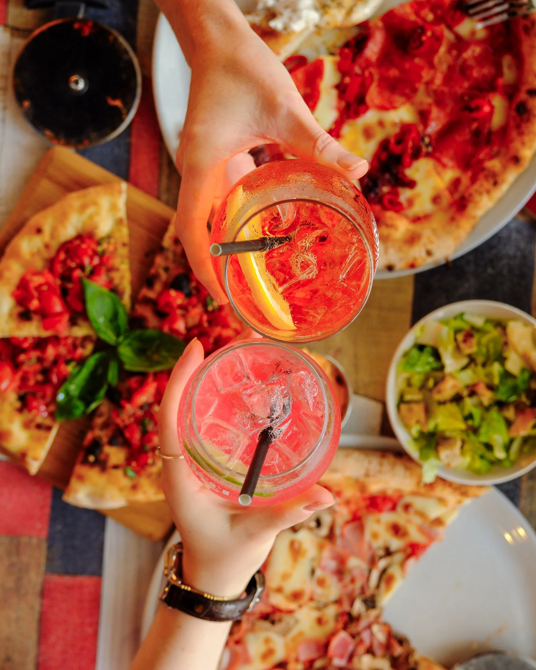 A person taking a photo of a pizza with a smartphone; the pizza has pepperoni slices and cheese, and there are glasses of red wine on the table.