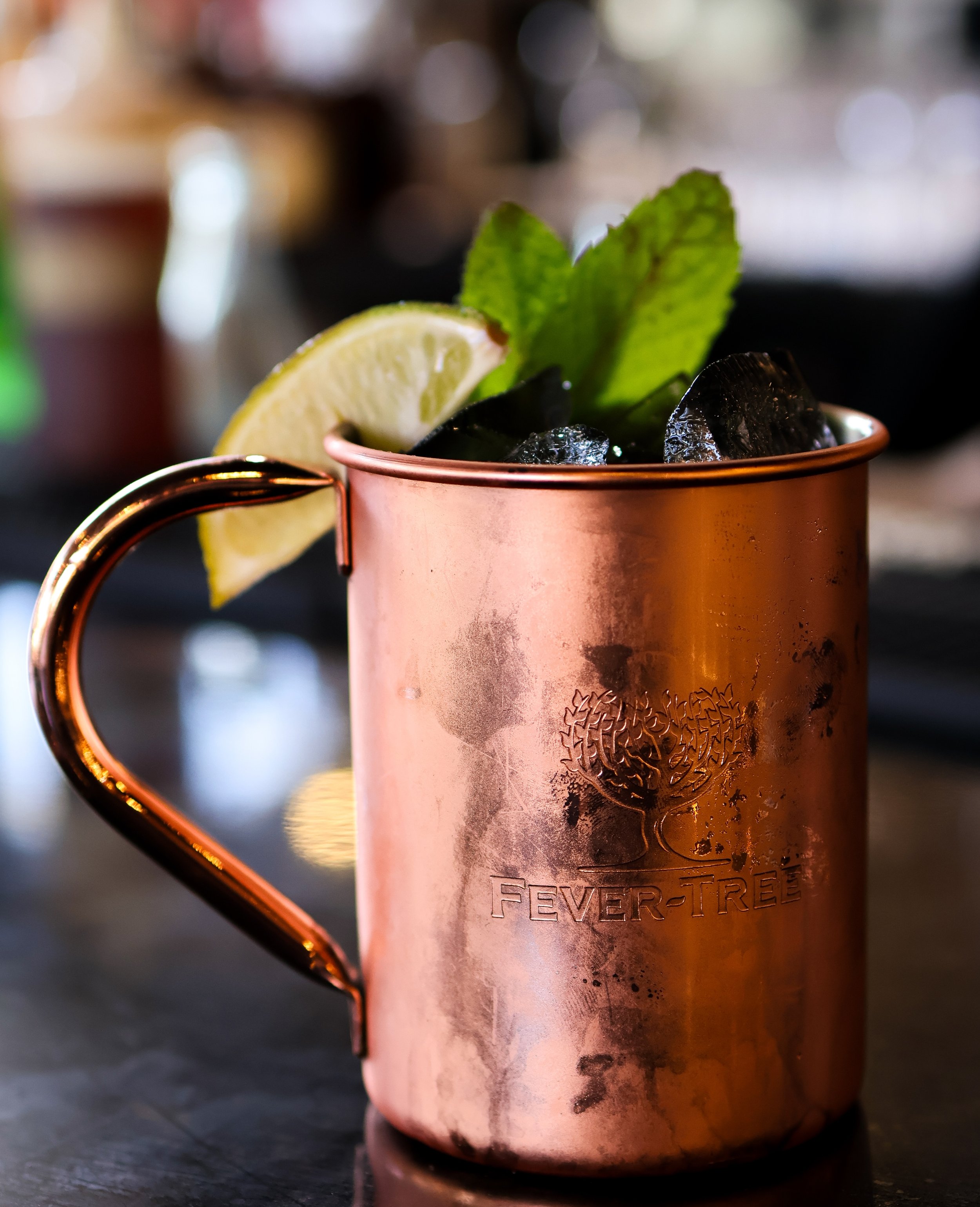 Copper mug filled with a cocktail, garnished with a lemon wedge and mint leaves, and ice cubes inside.