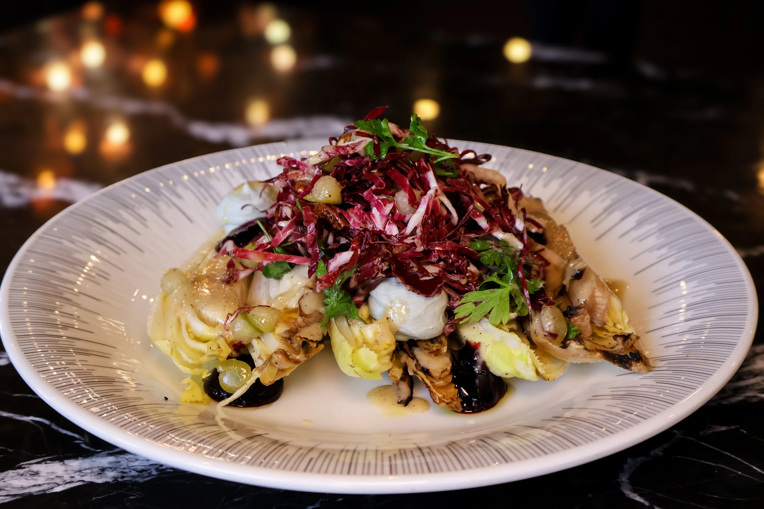 A plated dish with shredded red cabbage, greens, and various vegetables on a white patterned plate.