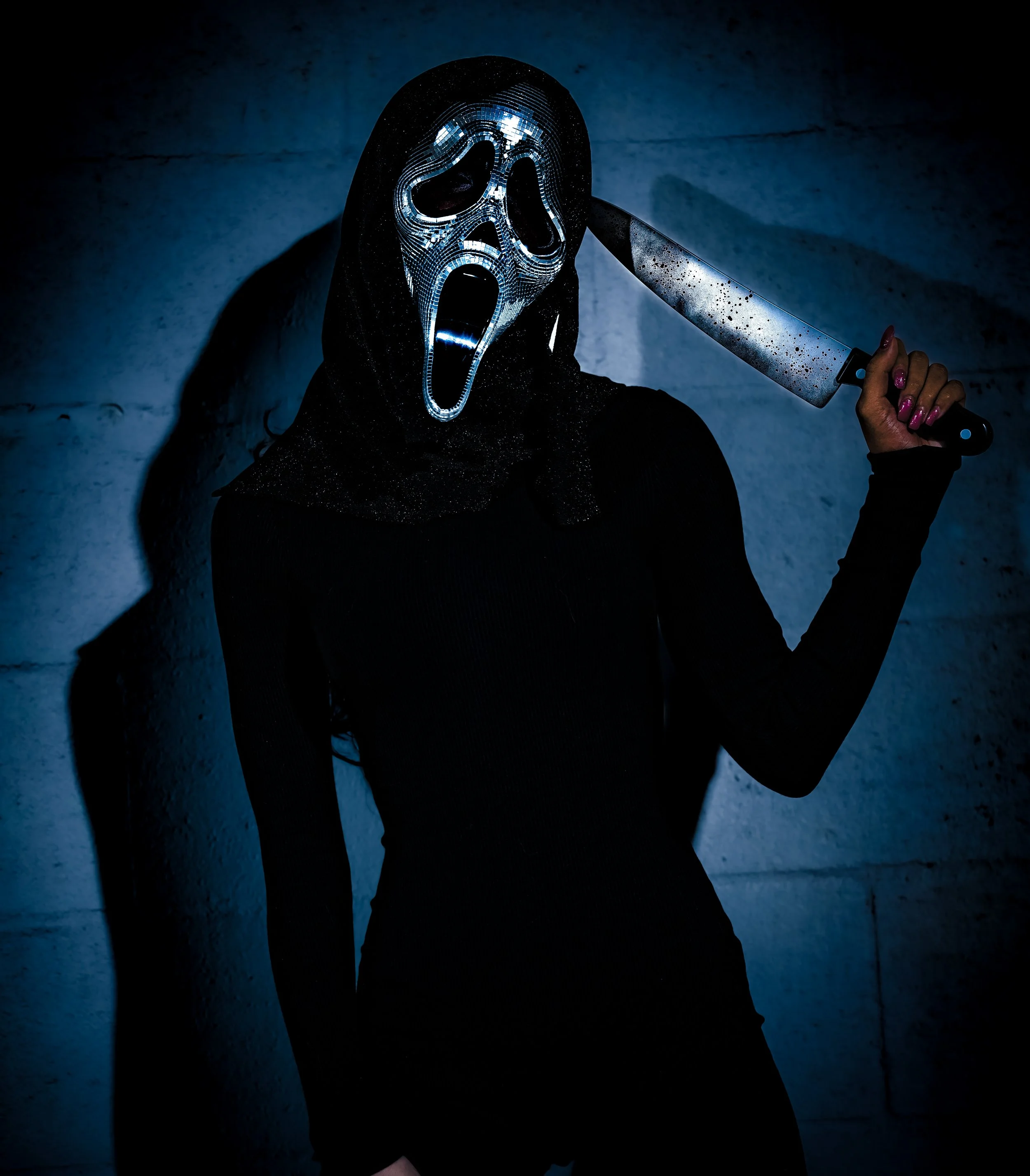 Person wearing a Ghostface mask from the movie Scream, holding a bloody knife, standing in a dark, moody setting.