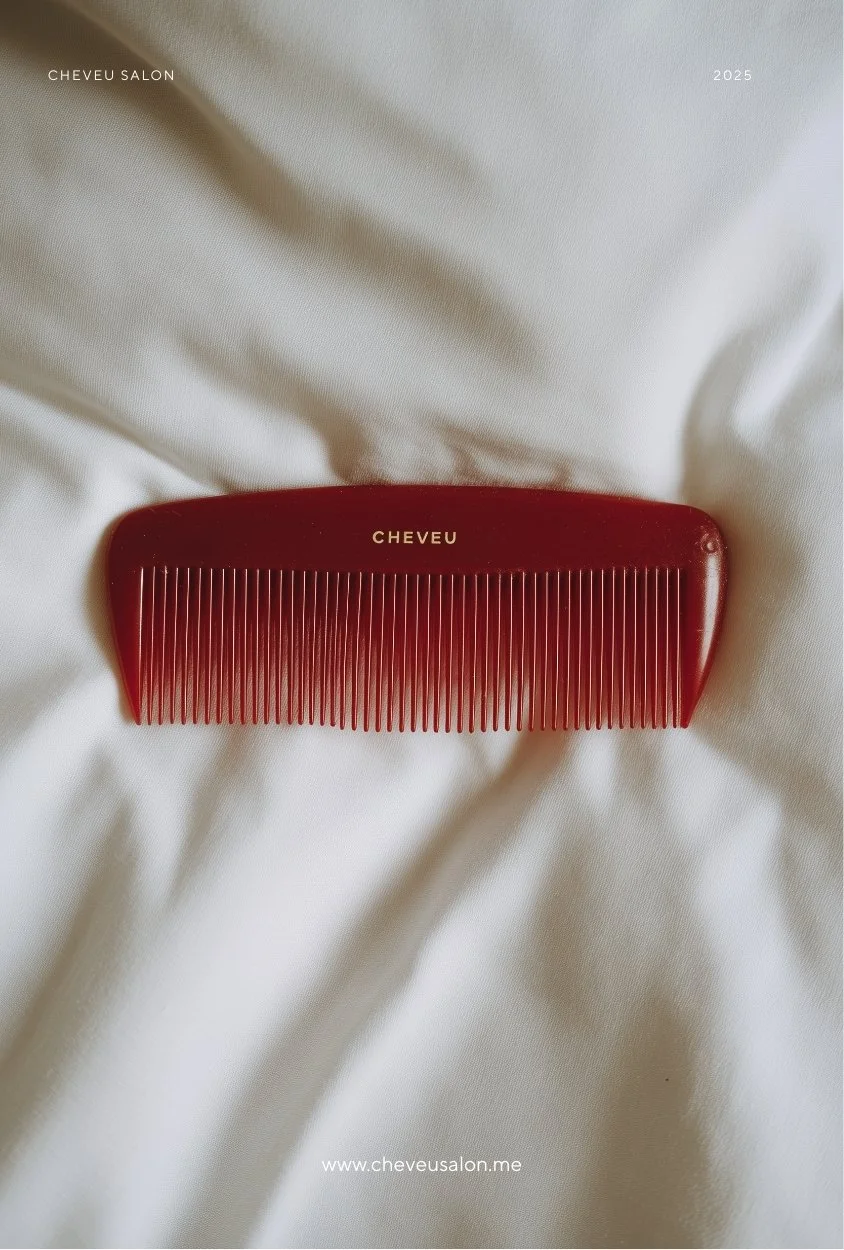 A red plastic hair comb with the brand name "CHEVEU" printed on it, placed on a white fabric surface.