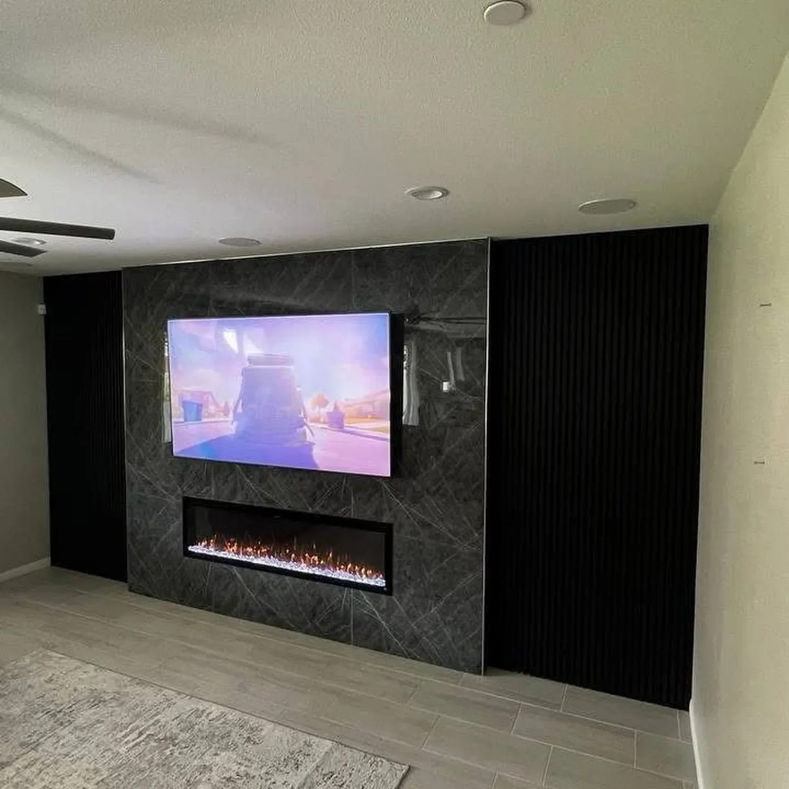 Living room with a wall-mounted TV, a modern fireplace beneath it, and dark paneling on the sides of the wall.