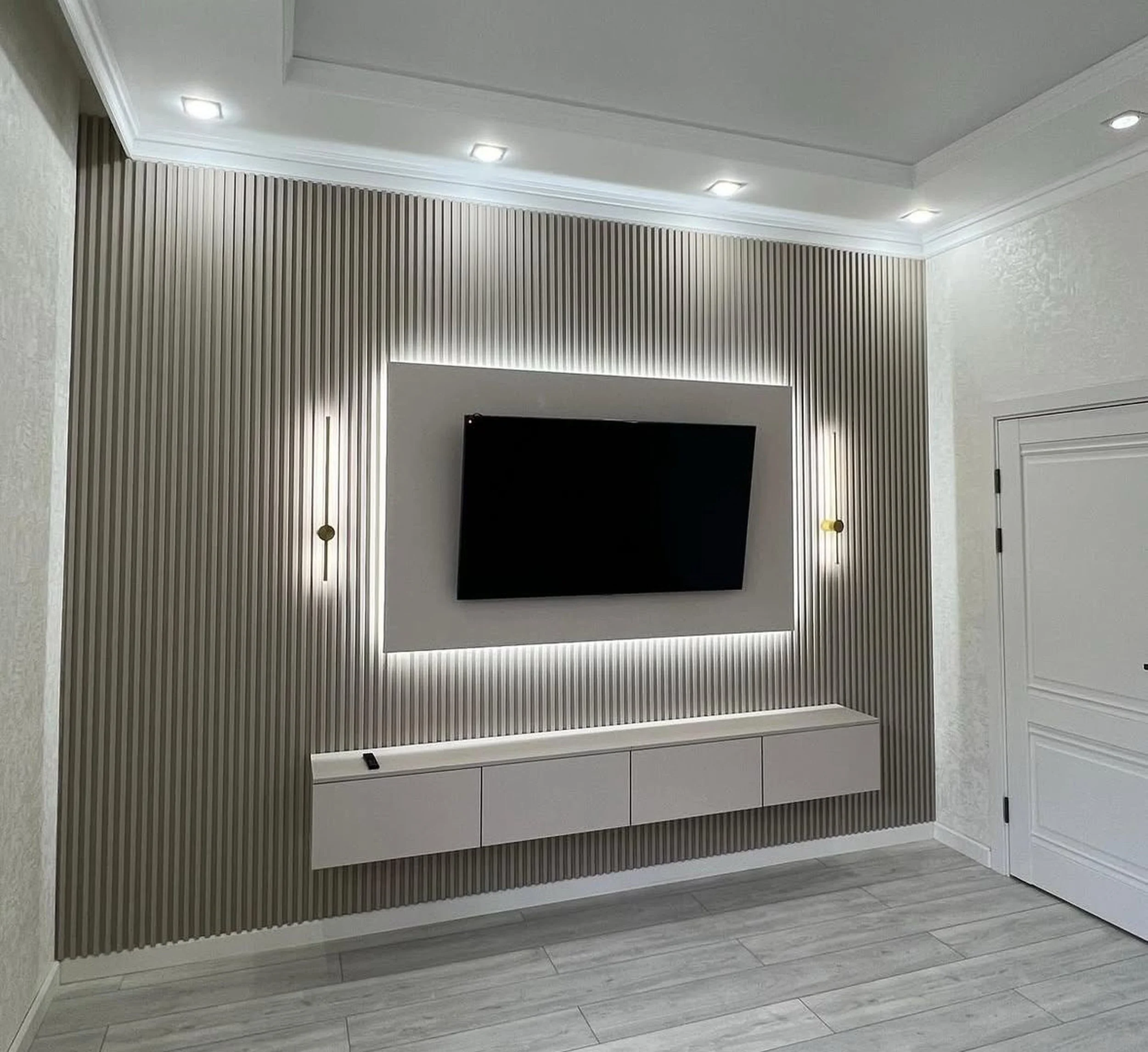 Modern living room wall with textured vertical stripes, a mounted flat-screen television, and a white floating cabinet below with backlit accents.