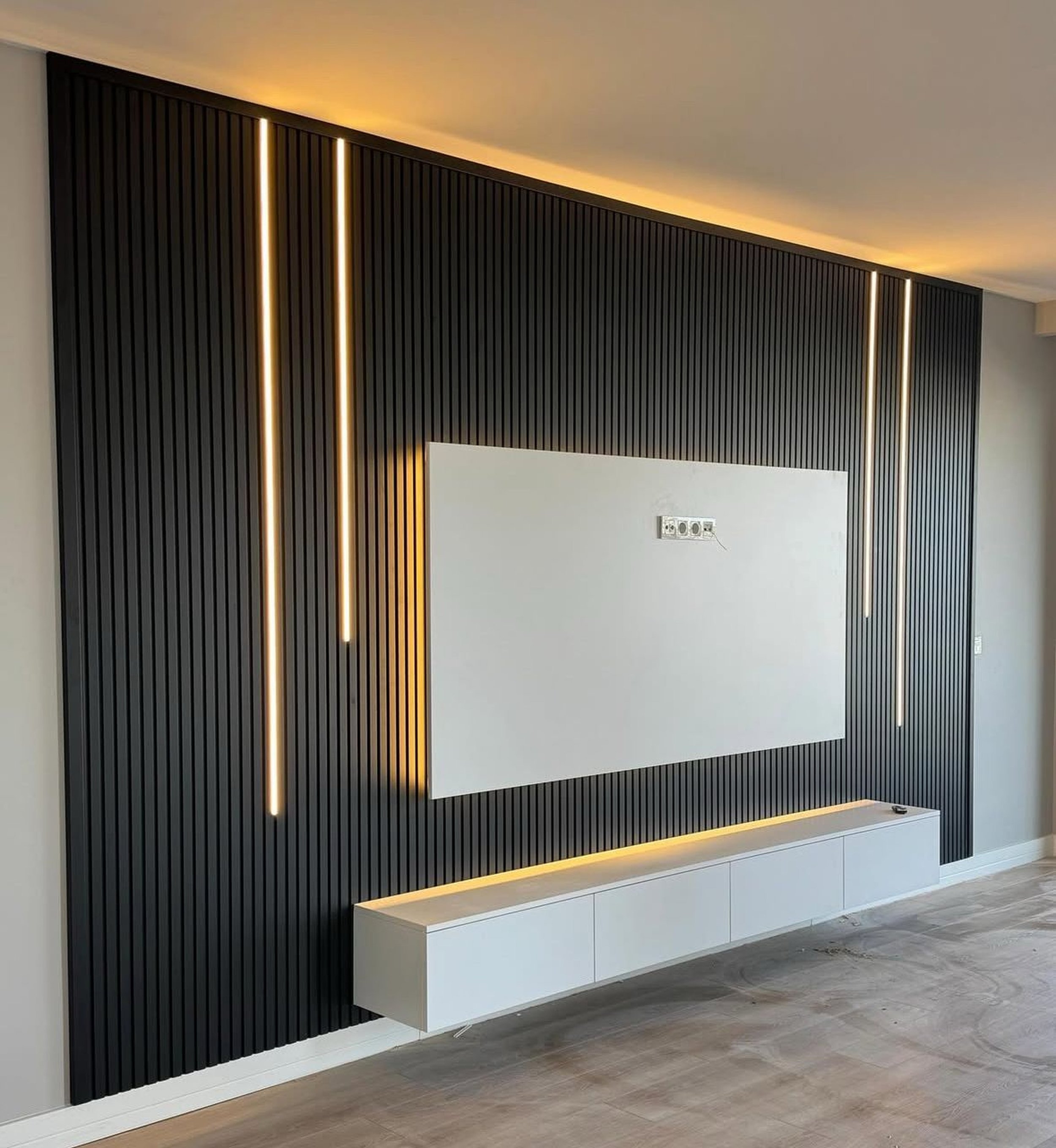 Modern interior wall with black vertical slats, integrated warm LED lighting, and a white floating cabinet beneath a blank white panel.