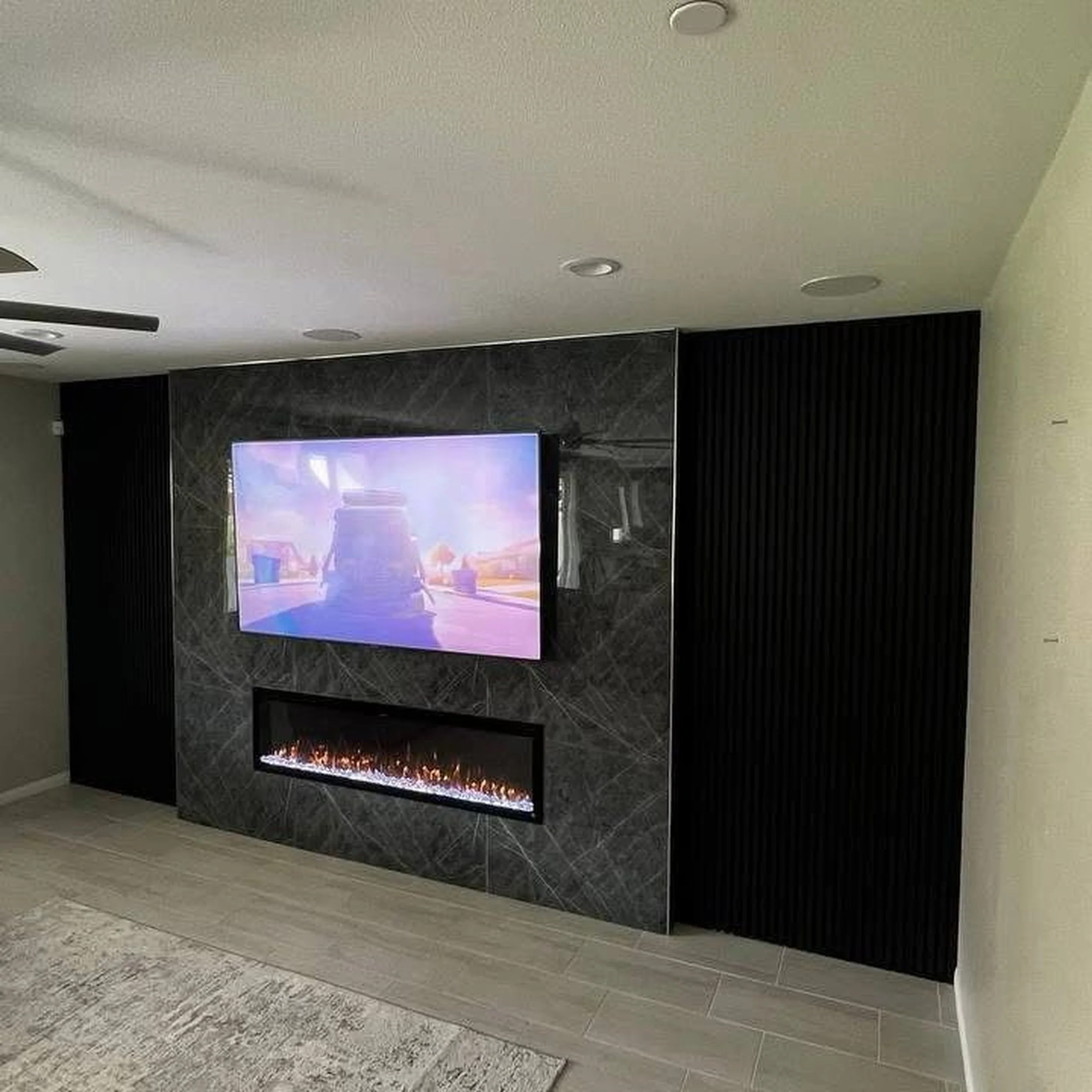 Living room with a wall-mounted TV, a modern fireplace beneath it, and dark paneling on the sides of the wall.