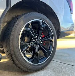 Close-up of a car wheel with a black alloy rim and a low-profile tire on a concrete surface.