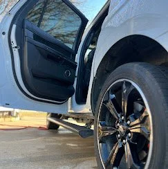 Open car door revealing interior, parked vehicle with black rim wheels, and tire.