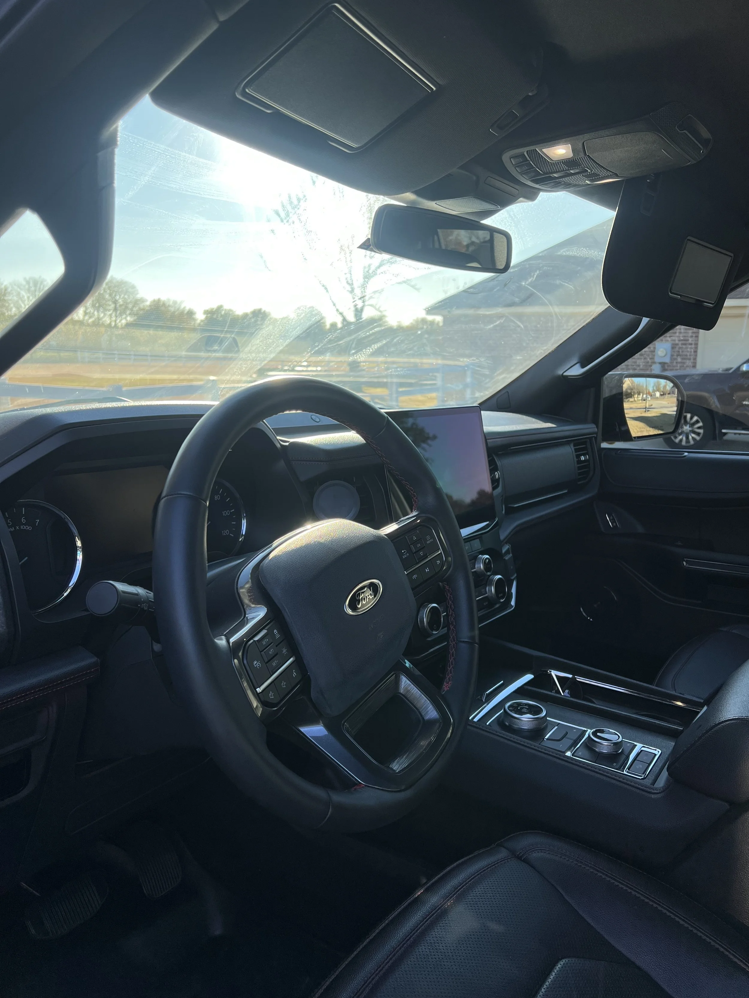 Interior of a Ford vehicle showing steering wheel, dashboard, and center console with gear controls, with sunlight streaming through the windshield.