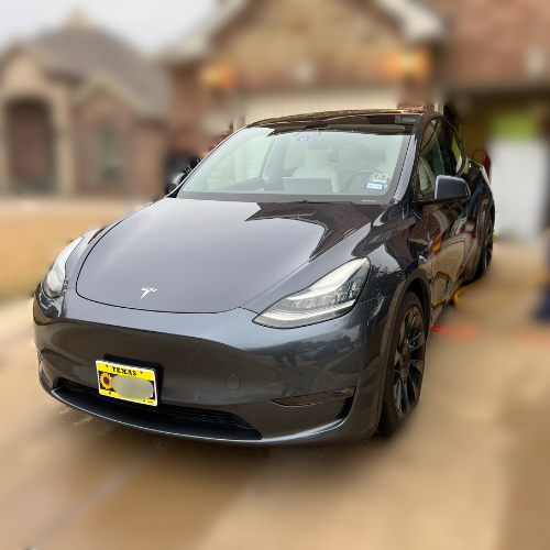 Black Tesla Model 3 parked in a driveway with a blurred residential house in the background.
