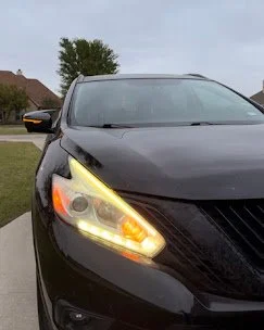 Black car with turned on headlights and daytime running lights parked on a residential street