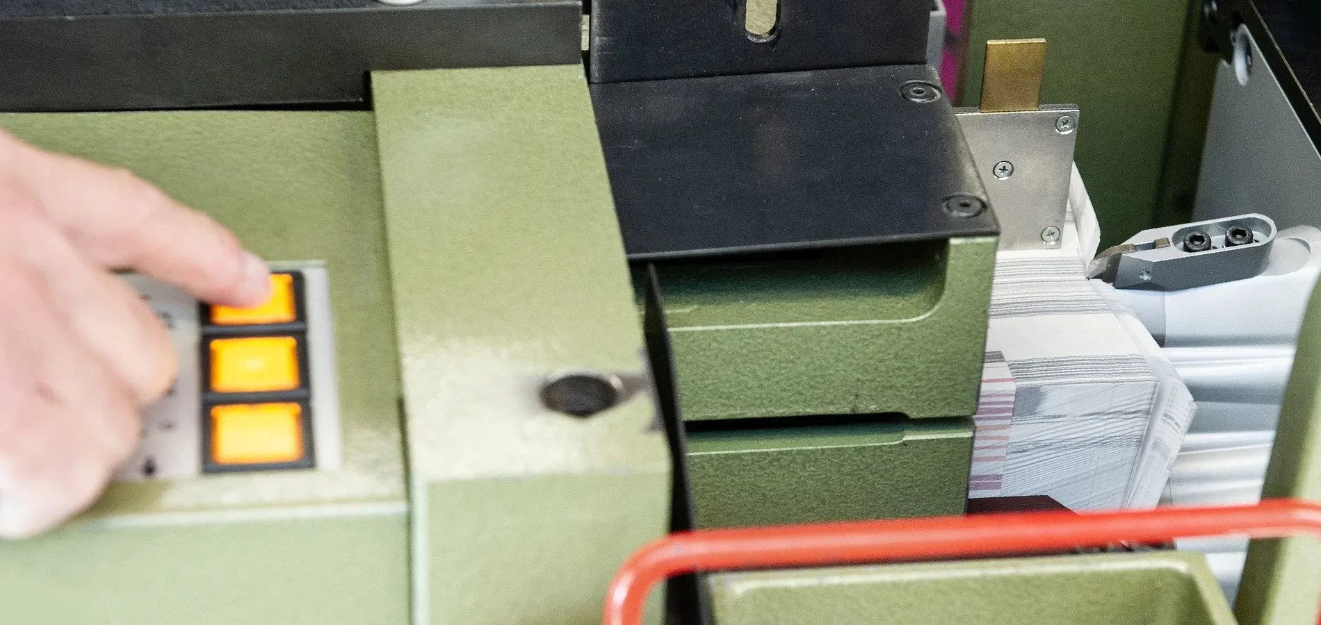 Close-up of a green printing machine with a person's hand pressing yellow buttons on a control panel.