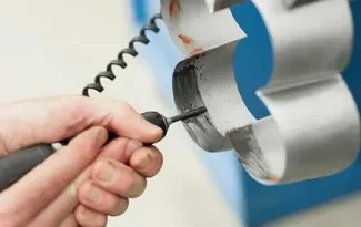 Close-up of a hand using a drill on a metallic object with a curved, shiny surface.