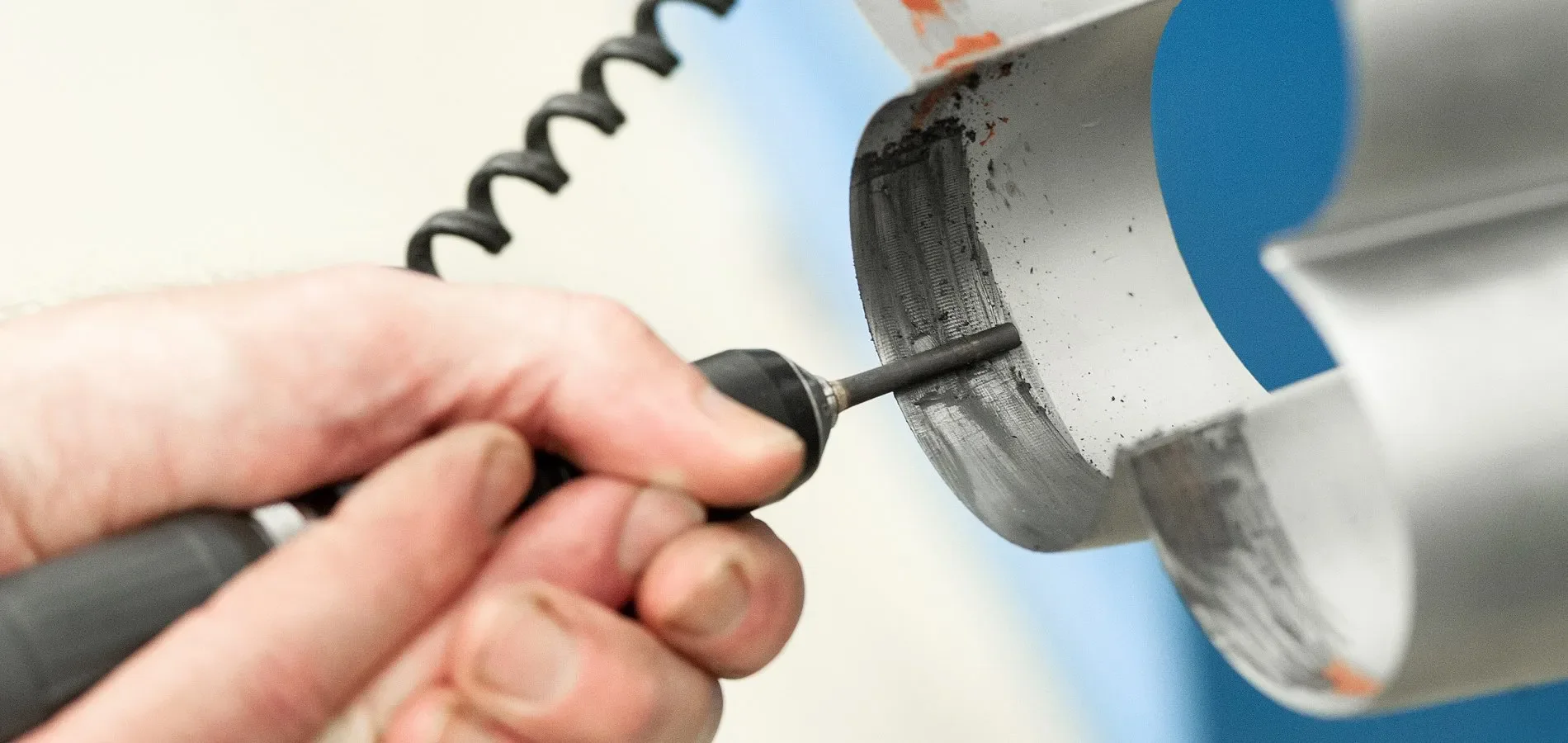 A hand holding a rotary tool is grinding or polishing the interior surface of a metal pipe or tube.