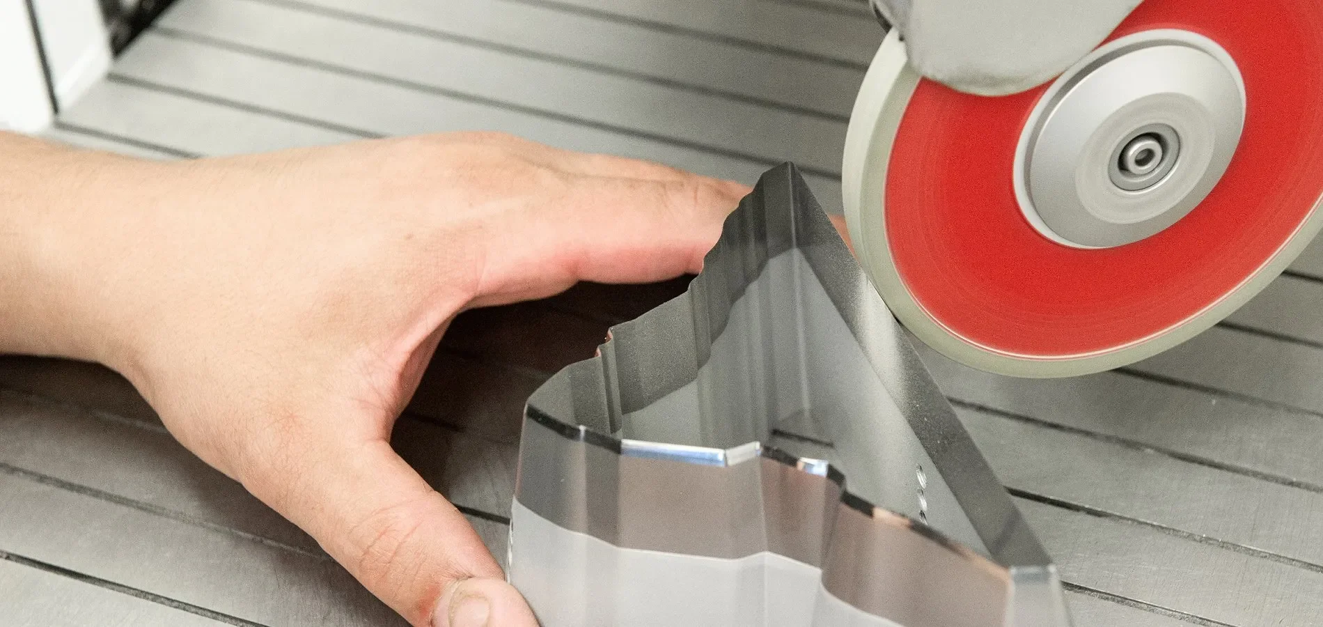 Close-up of a hand guiding a metal sheet through a red and silver rotary cutting saw on a metal workbench.