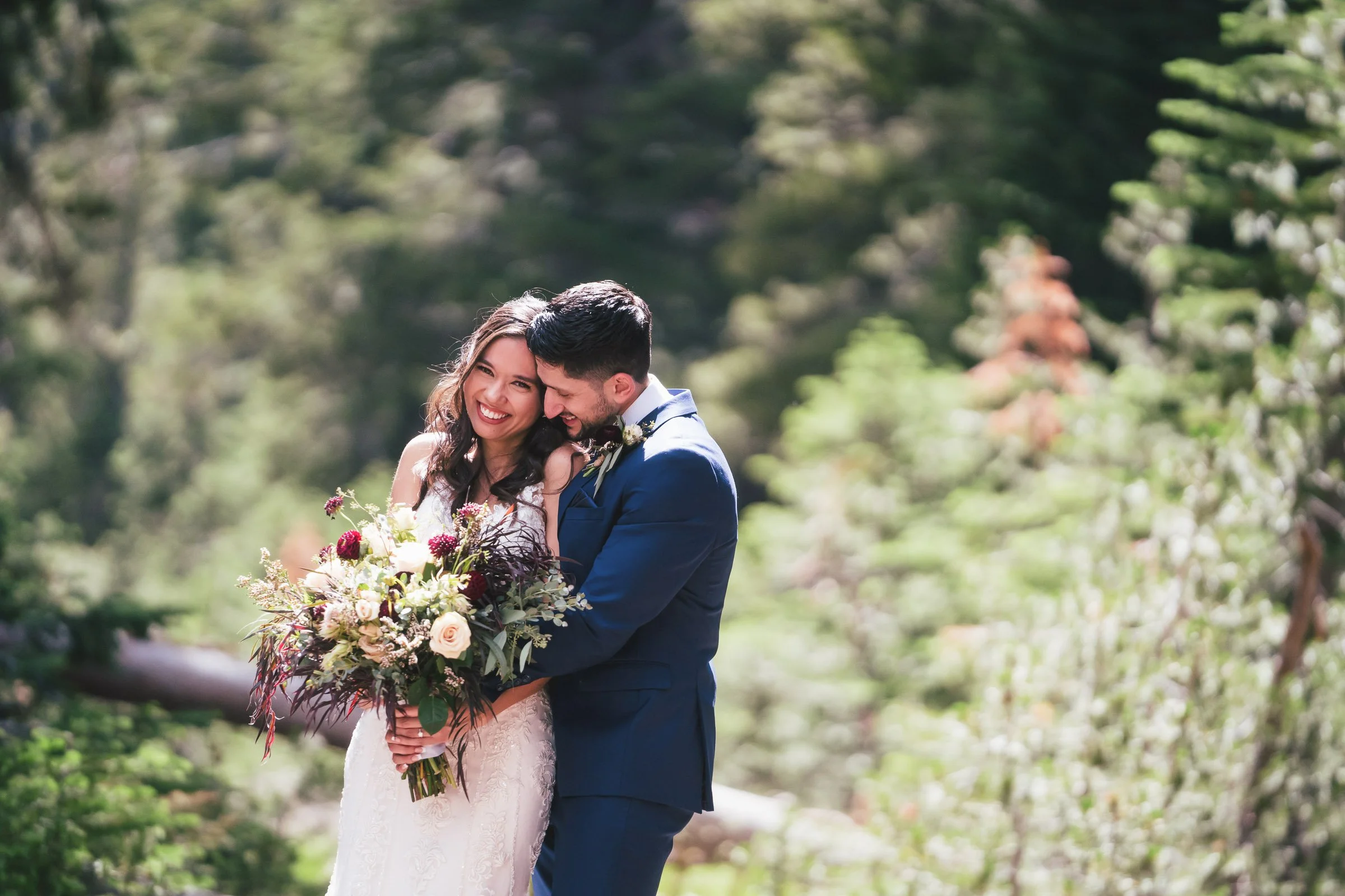 A newlywed couple in wedding attire sharing a joyful moment outdoors, with the bride holding a large bouquet of flowers and both smiling.