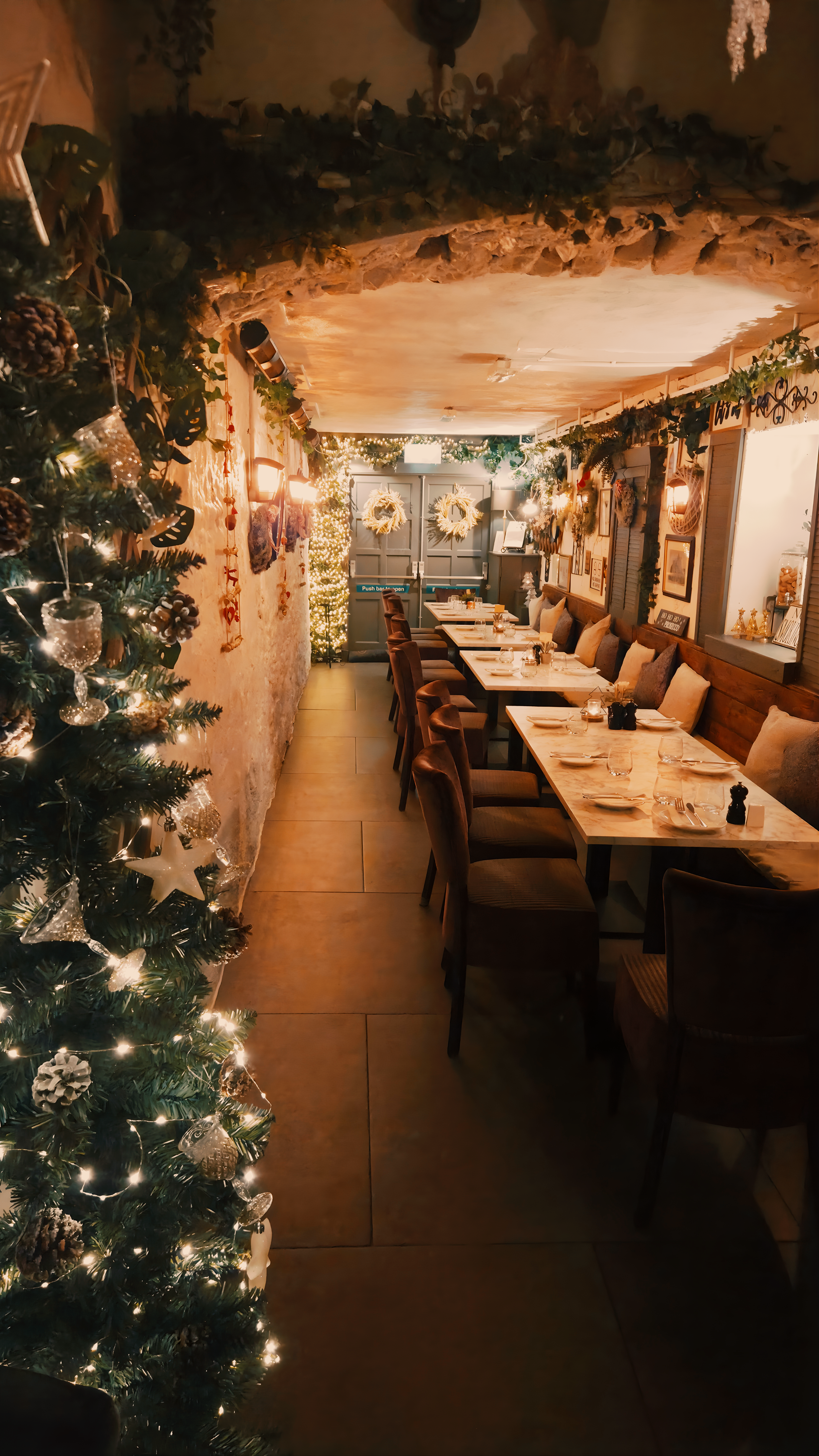 Cozy restaurant decorated for Christmas with a decorated Christmas tree on the left, string lights, and festive wreaths.