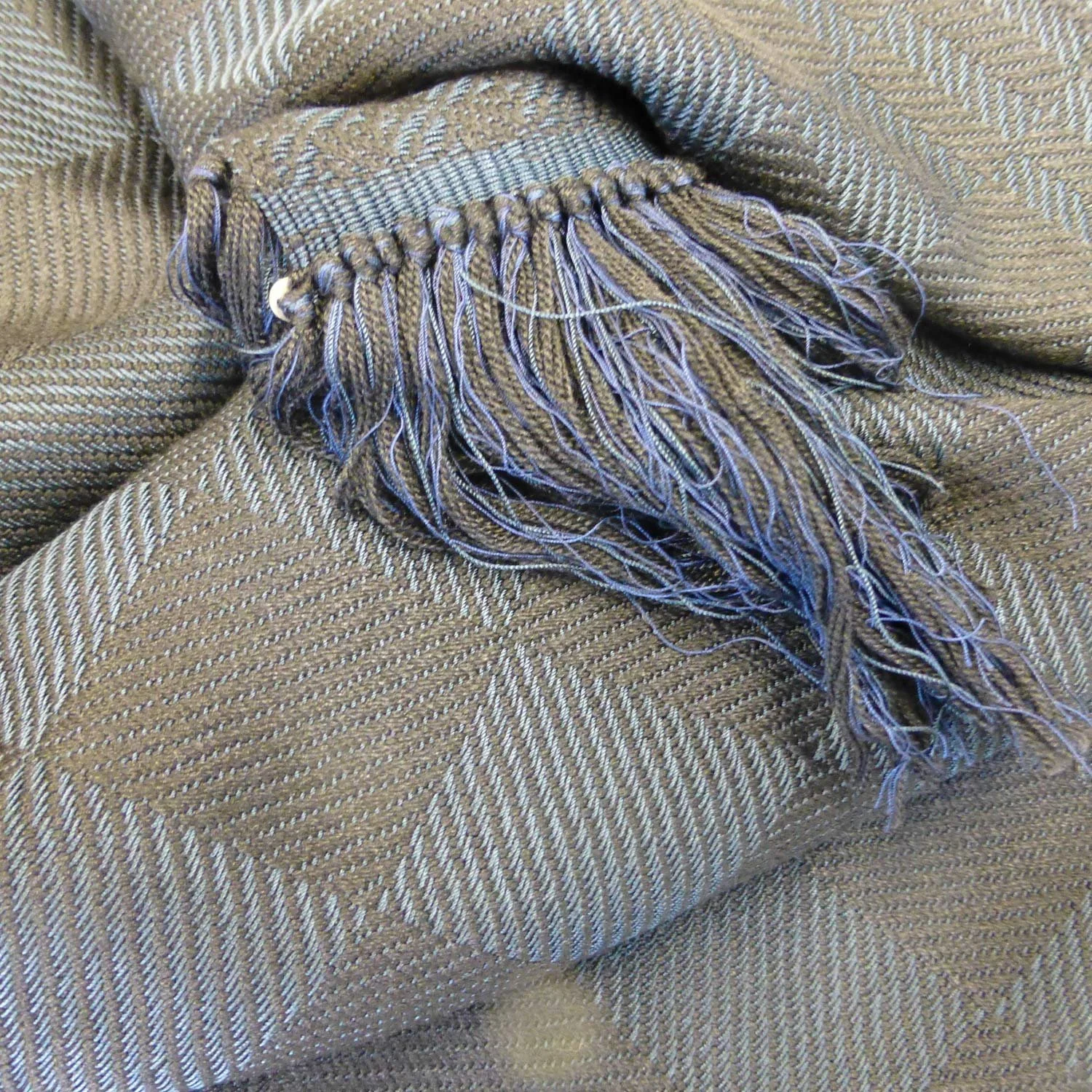 Ein beige-braunes Tuch mit Fransen liegt aufgefaltet auf einer Oberfläche.