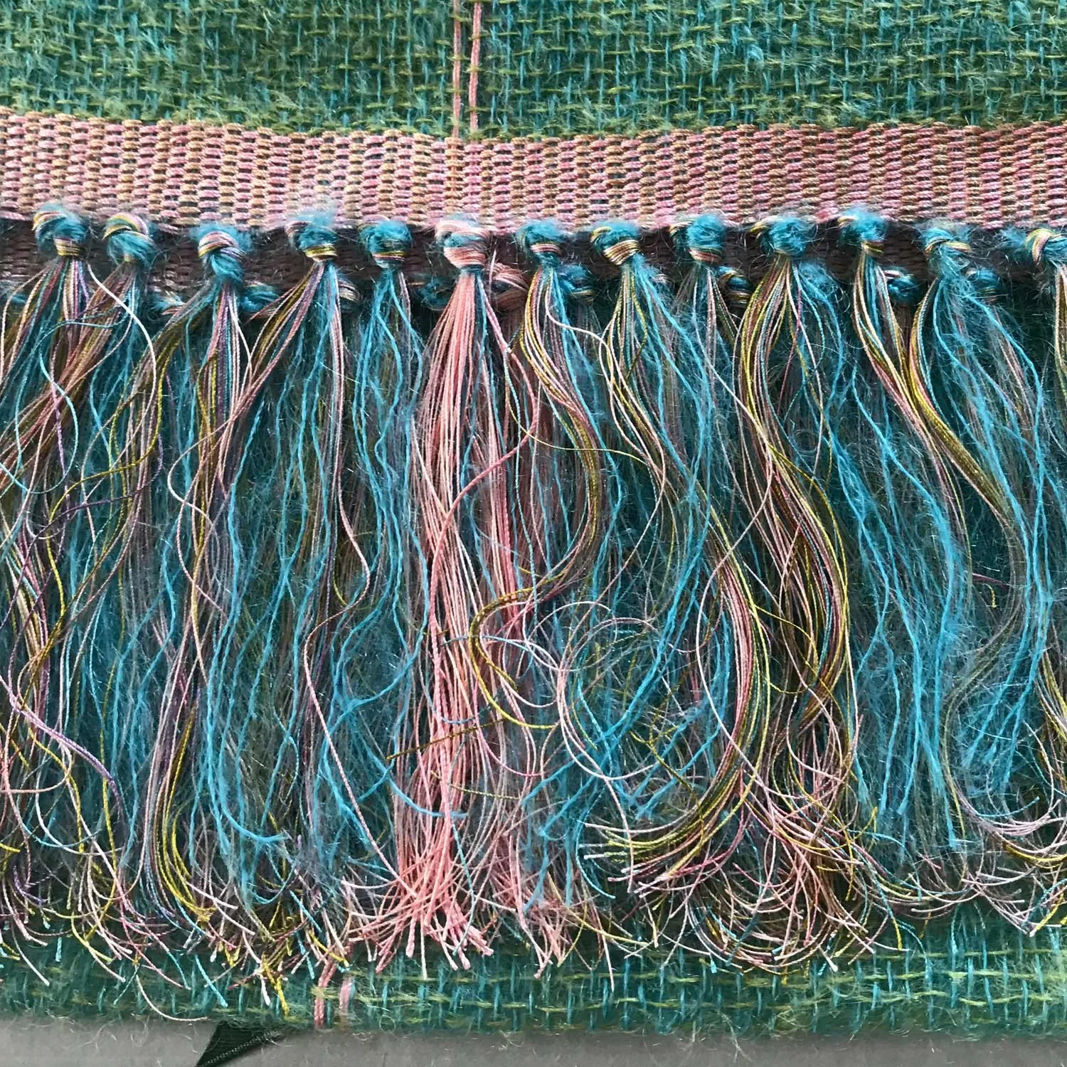 Nahaufnahme eines geflochtenen, bunt bestickten Textilstoffs mit langen, bunten Fransen.