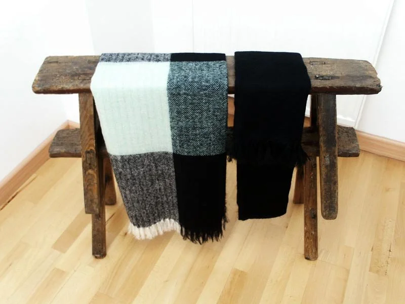 Ein alter Holztisch mit zwei handgefertigten Wollschals, einer in Schwarz-Weiß und der andere in Schwarz, die auf dem Tisch hängen.