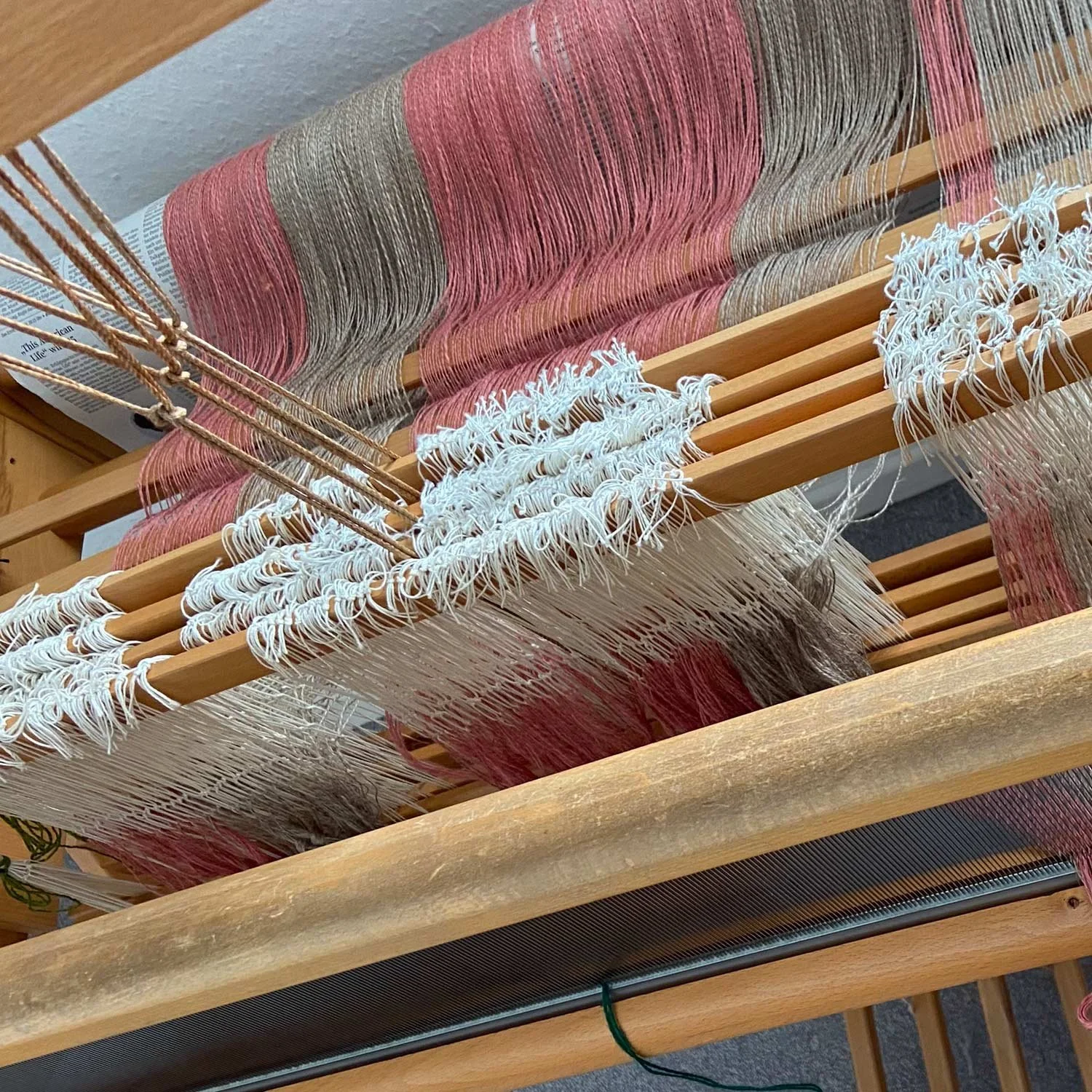 Nahaufnahme eines handgewebten Tapestries auf einem Webrahmen, die Garnrollen sind in Rot, Schwarz und Beige gefärbt.