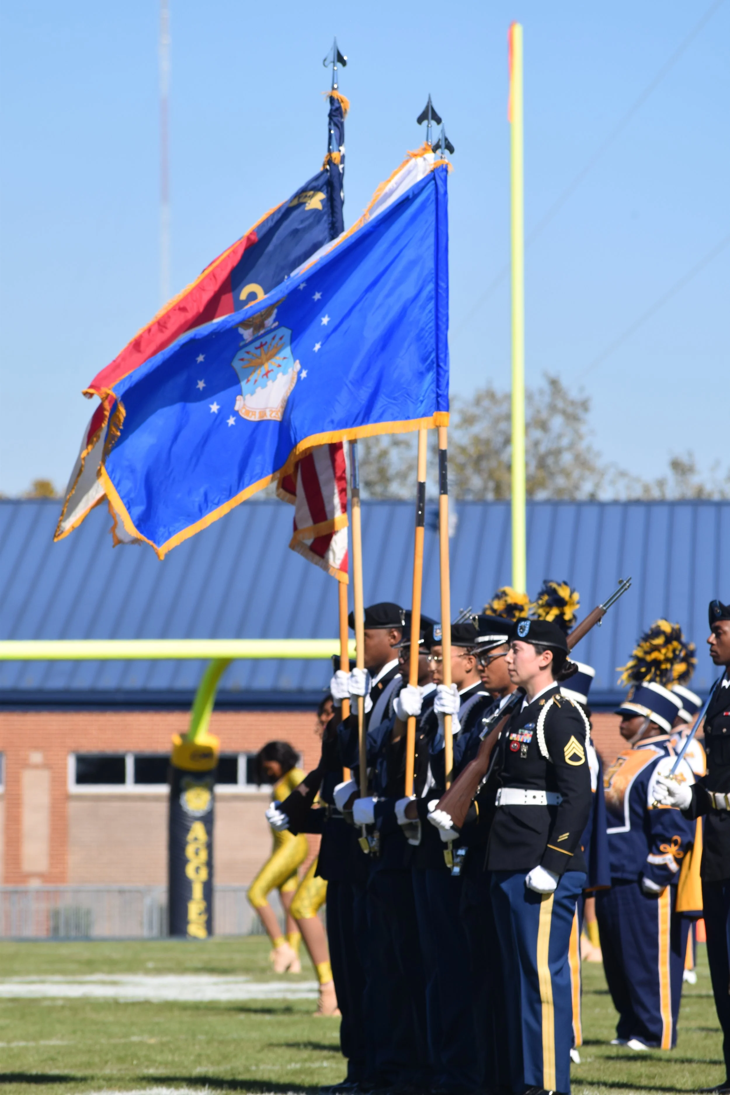 Military honor guard standing in formation on a football field, holding flags including the Nevada state flag and the American flag, during a ceremony.