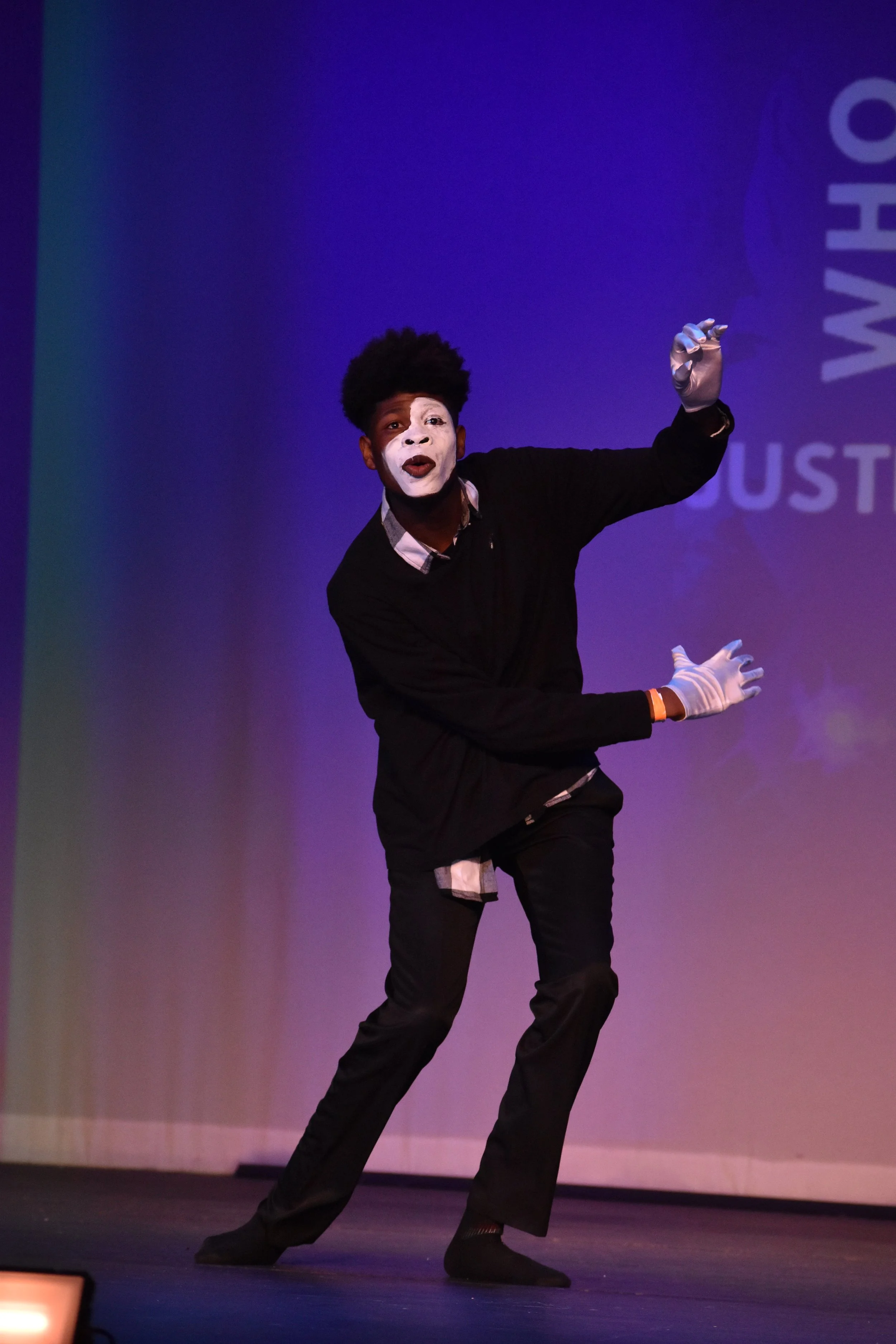 A mime performs on stage with a colorful background.