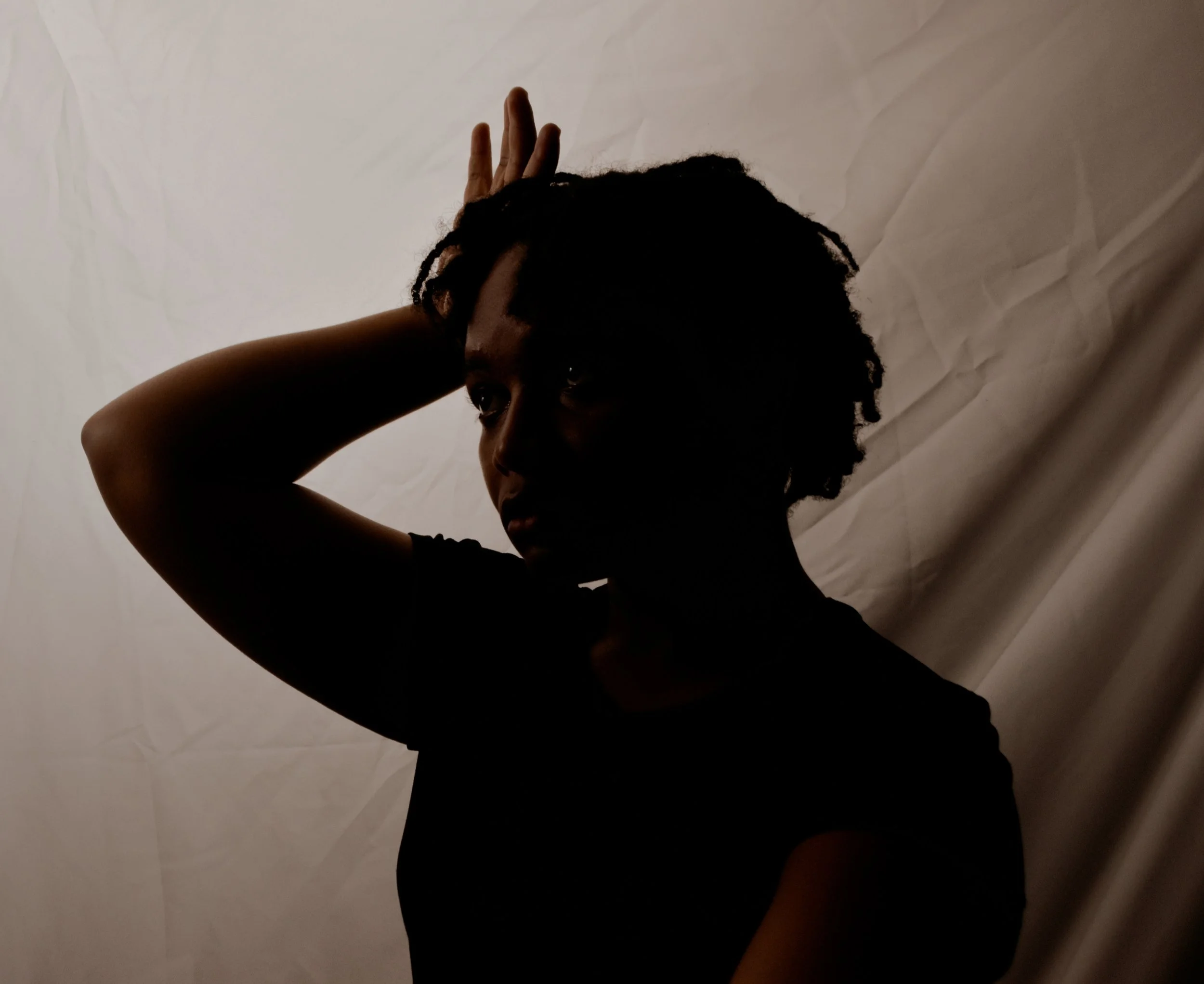Silhouette of a woman with her hand on her head, dark background, light behind her.