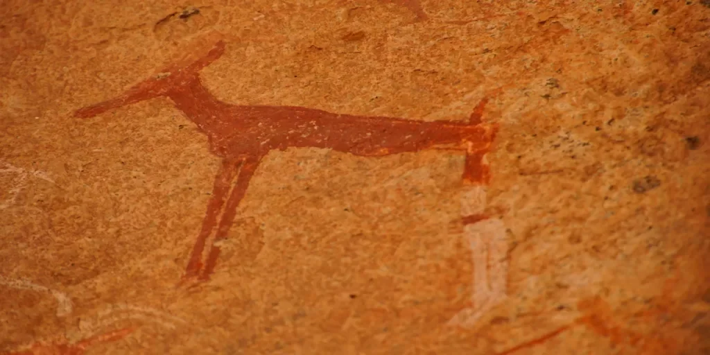 Ancient cave painting of a reindeer on a reddish-brown wall.